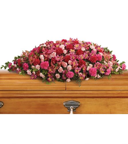 Pink and red floral casket spray on a wooden casket