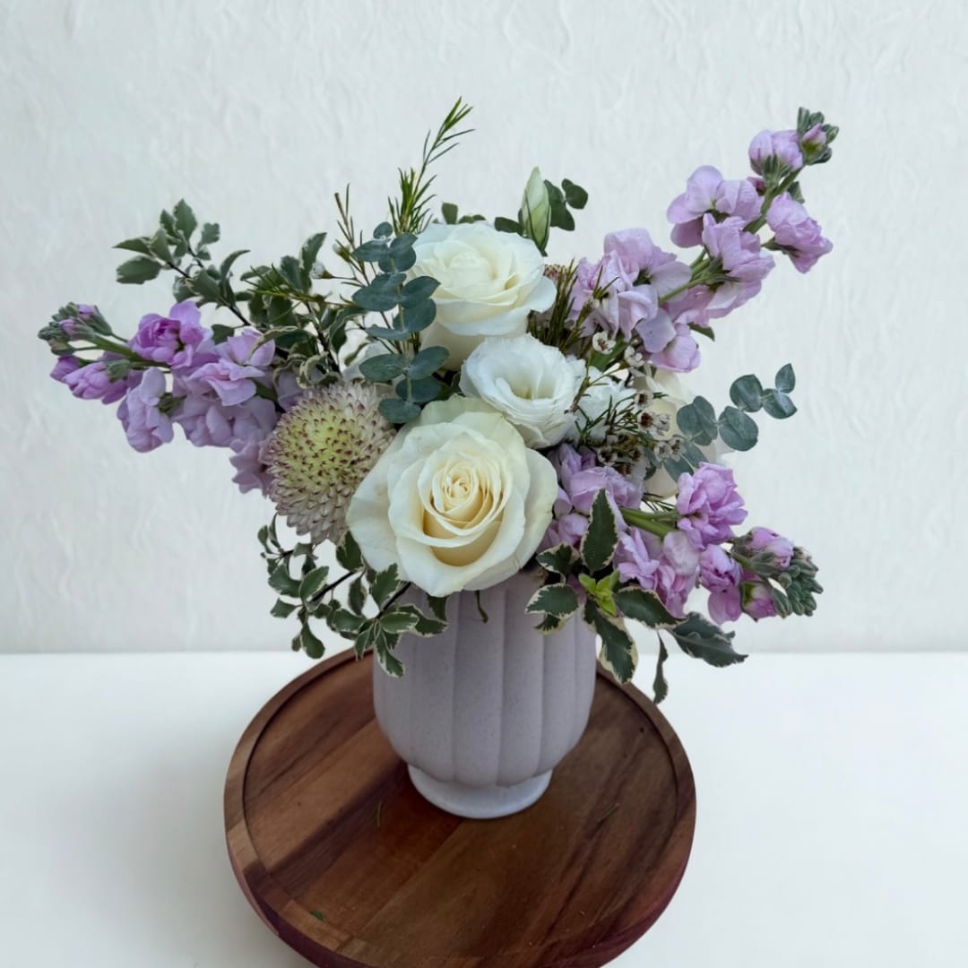 White roses and lavender flowers in a ribbed vase on a wooden tray