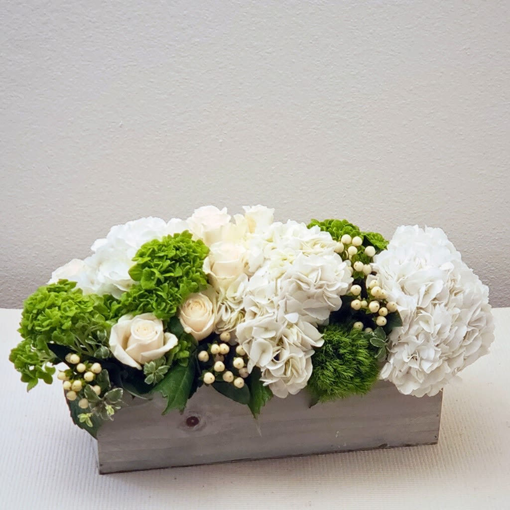 The Hamptons - Experience the classic beauty of our Hamptons Vintage Box arrangement. This elegant design features a textured blooms blend of roses, dianthus, and hydrangeas in soft, complementary hues of green and white. Presented in a rustic wooden box, it's the perfect centerpiece for any occasion. Add water daily to keep blooms fresh.