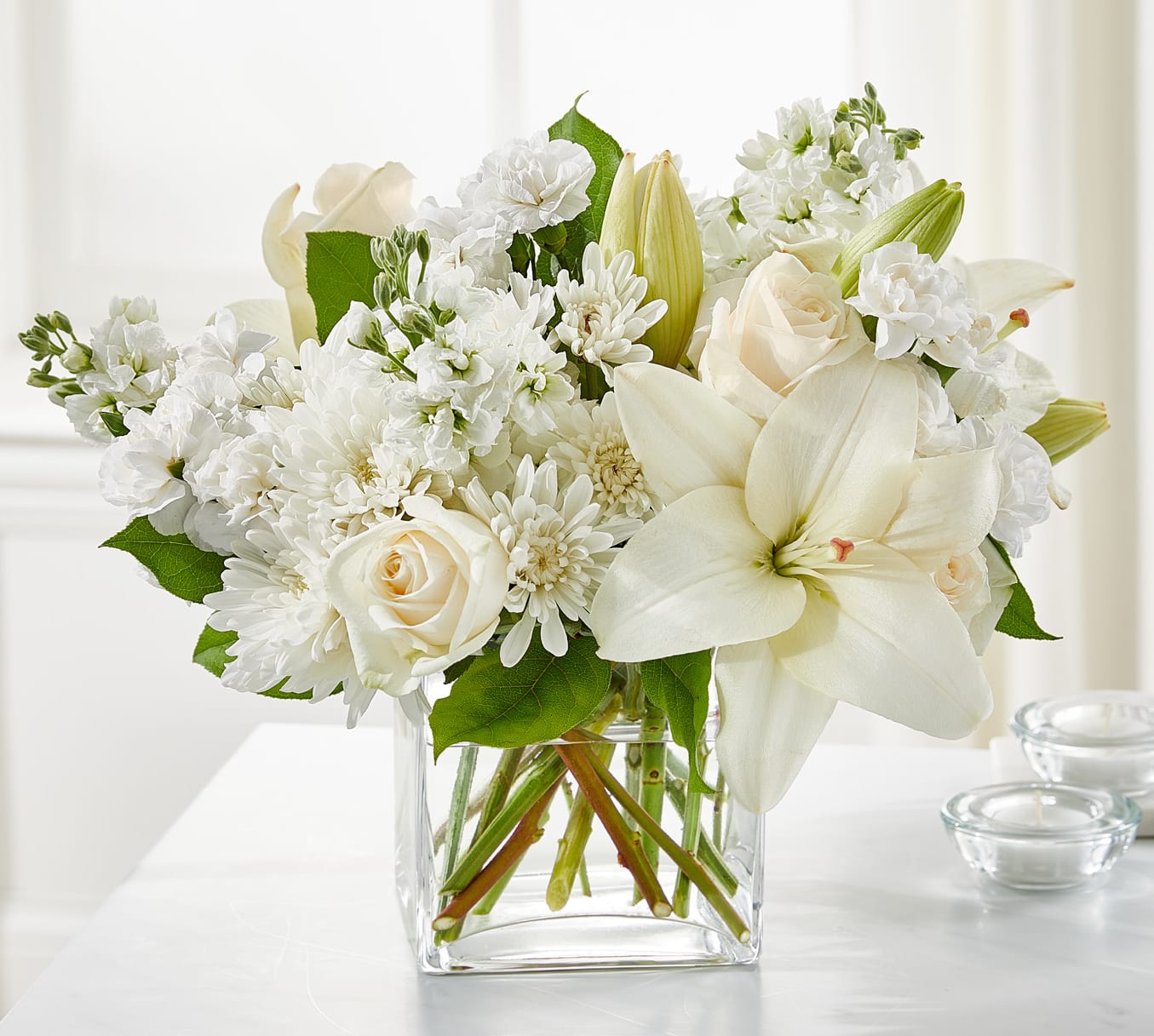 White floral arrangement in a clear glass vase with roses and lilies