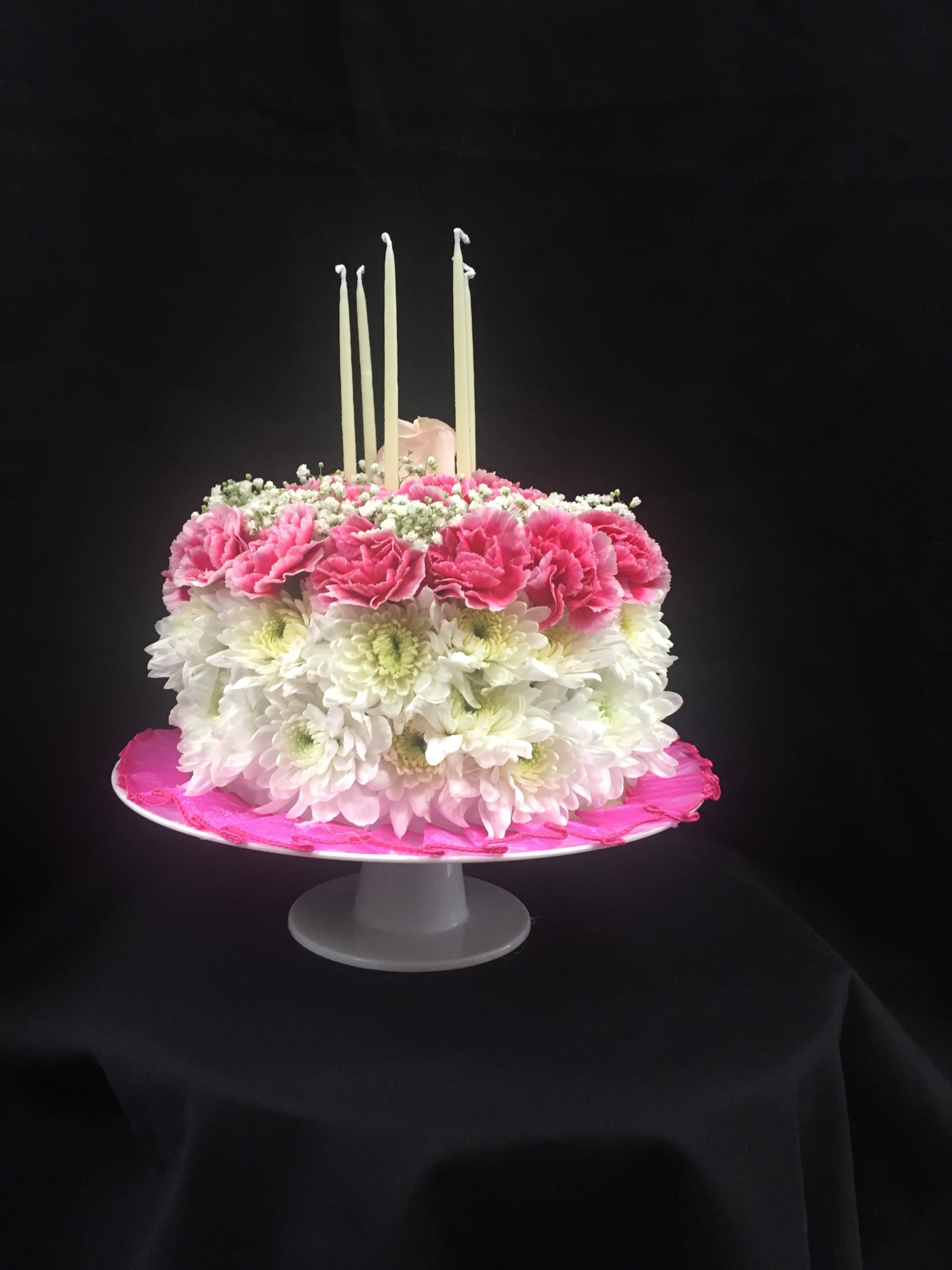 Pink and white floral cake with tall candles on a pedestal stand