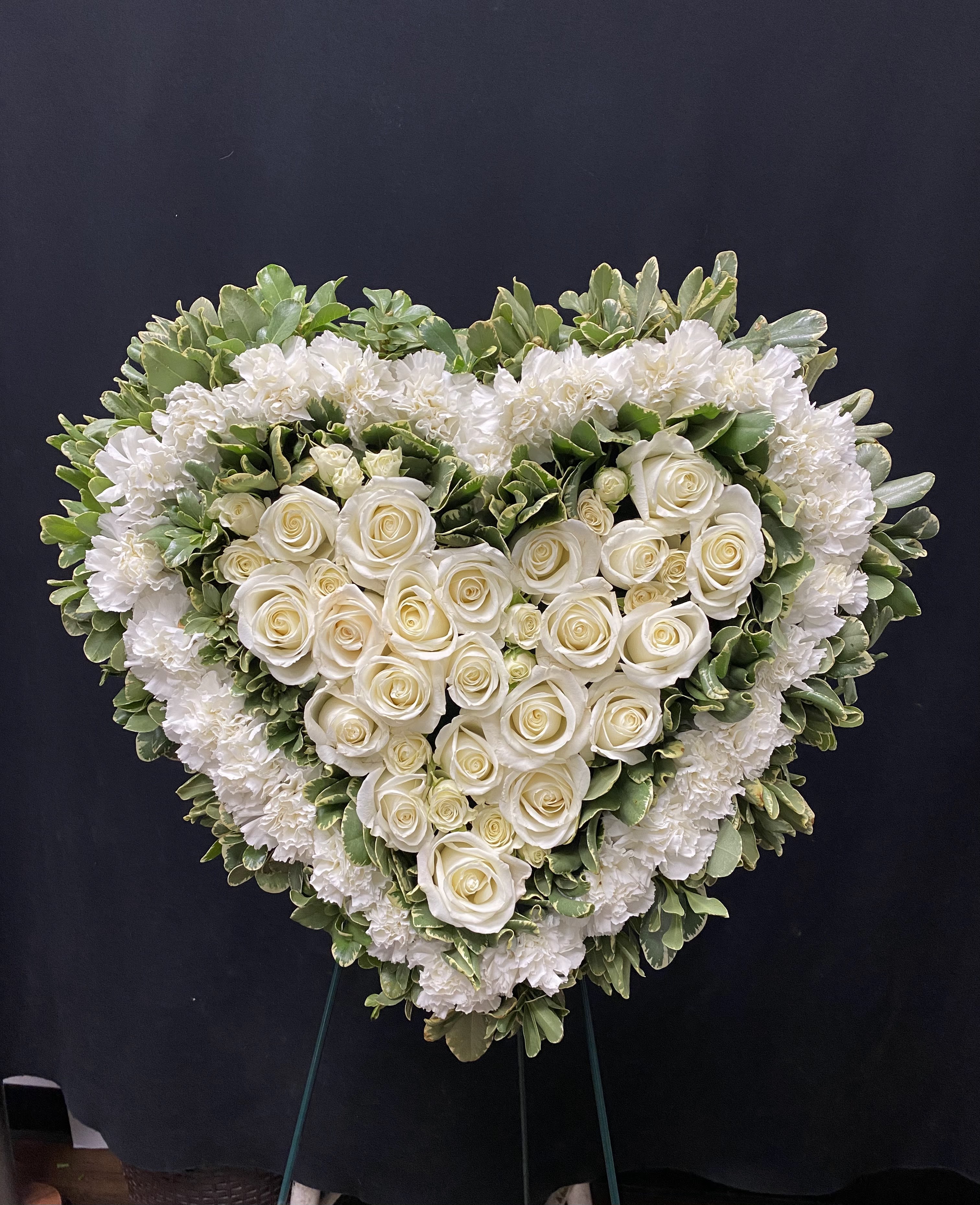 Heart-shaped white rose and carnation funeral spray on a stand