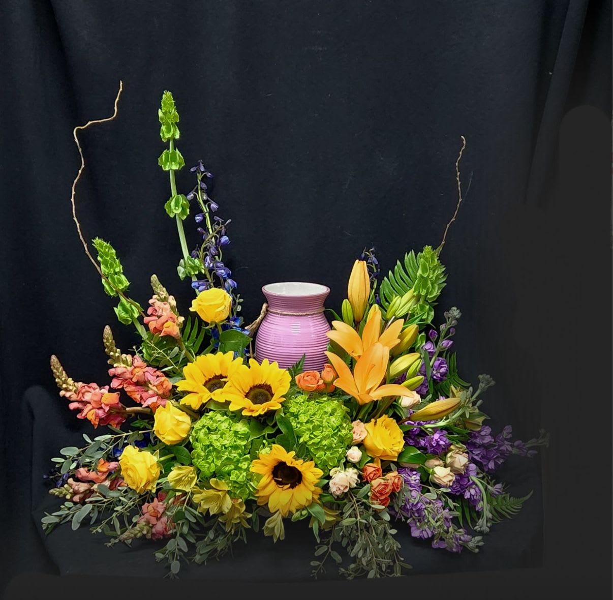 Colorful floral arrangement with sunflowers, lilies, and a purple vase