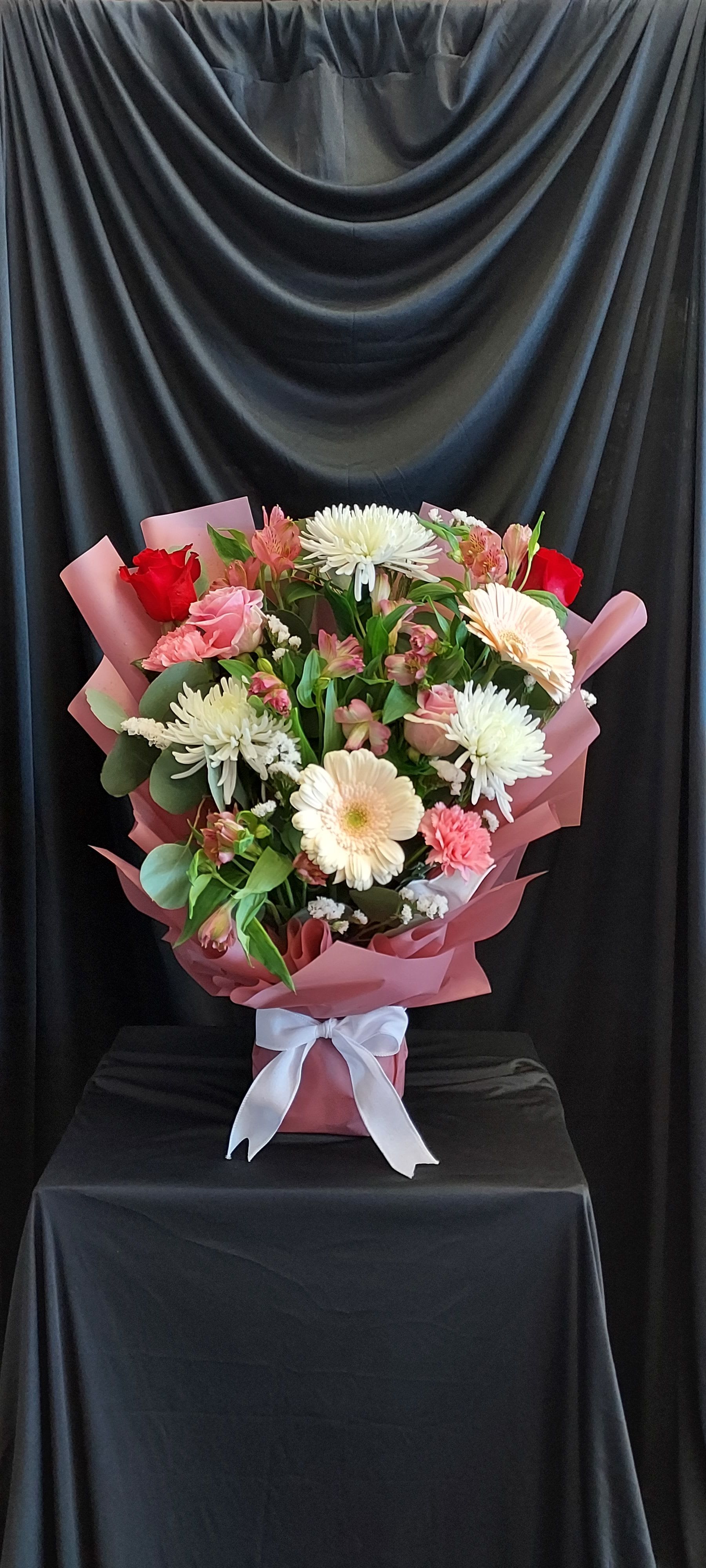 Mixed bouquet of pink and white flowers wrapped in pink paper with a white ribbon