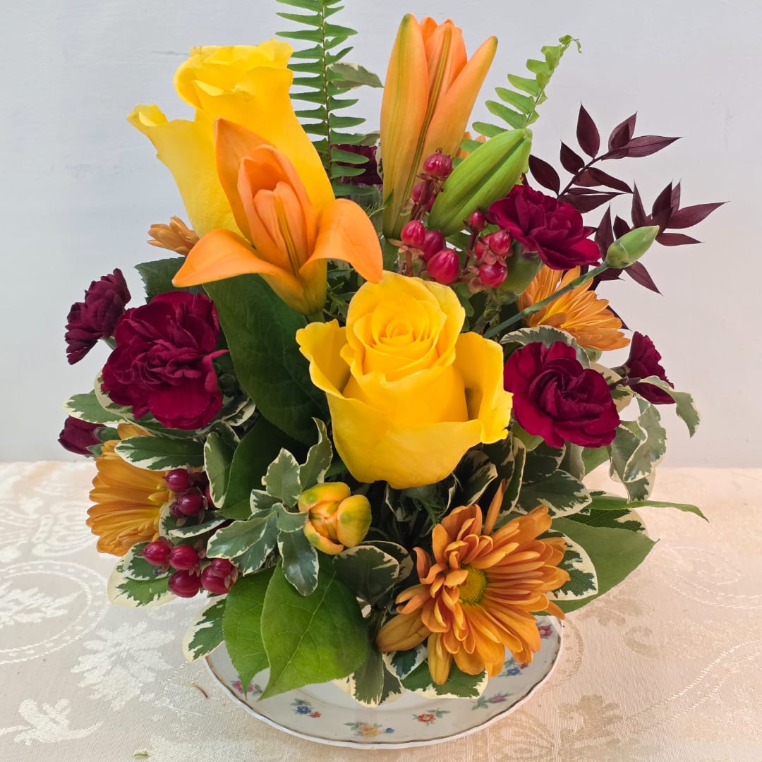 Mixed bouquet with yellow roses, orange lilies, and burgundy flowers in a floral teacup