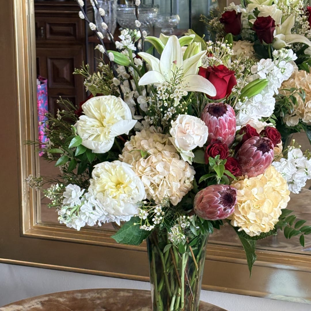 Mixed bouquet with white lilies, red roses, hydrangeas, and protea in a glass vase