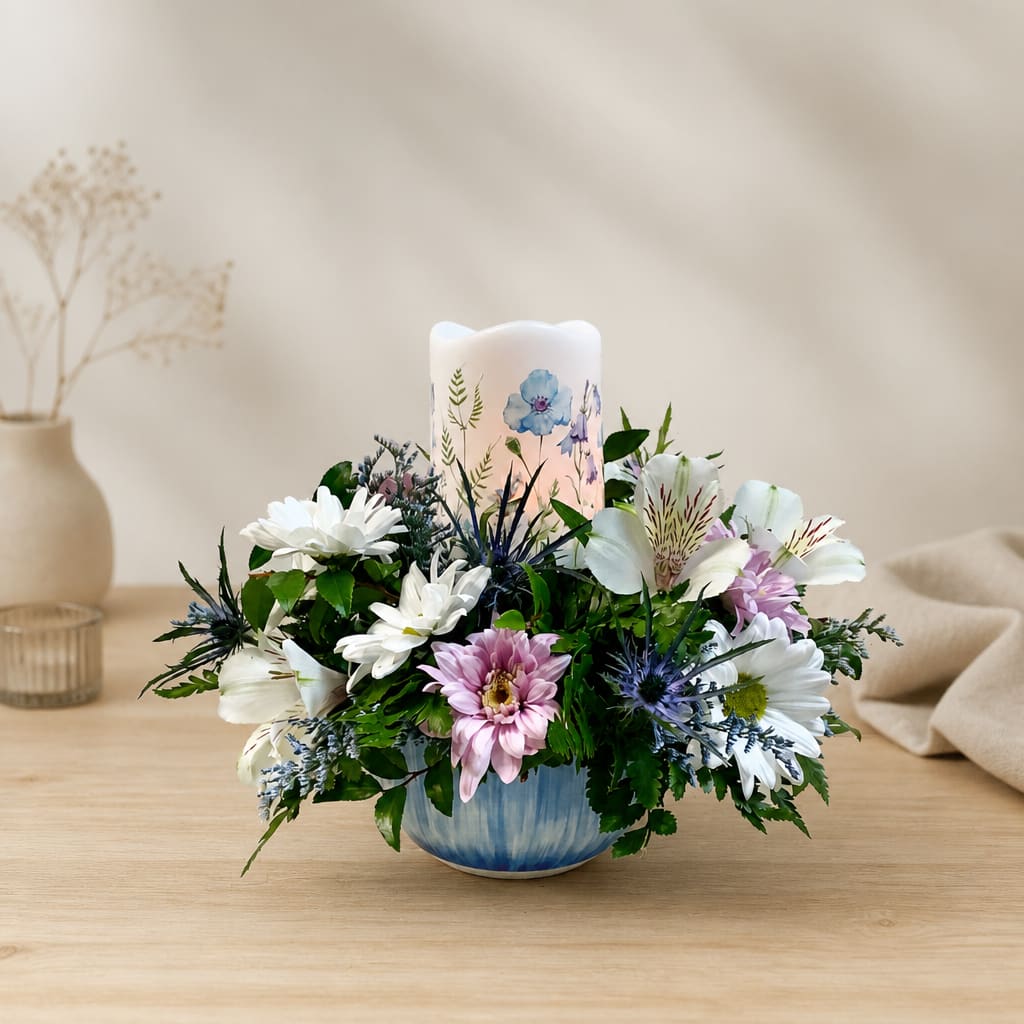 Mixed white and pink flowers arranged around a candle in a blue bowl