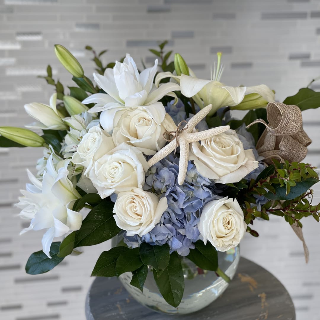 White roses and lilies arranged with blue hydrangeas in a glass vase