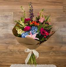 Mixed bouquet of colorful flowers wrapped in brown paper with a white ribbon