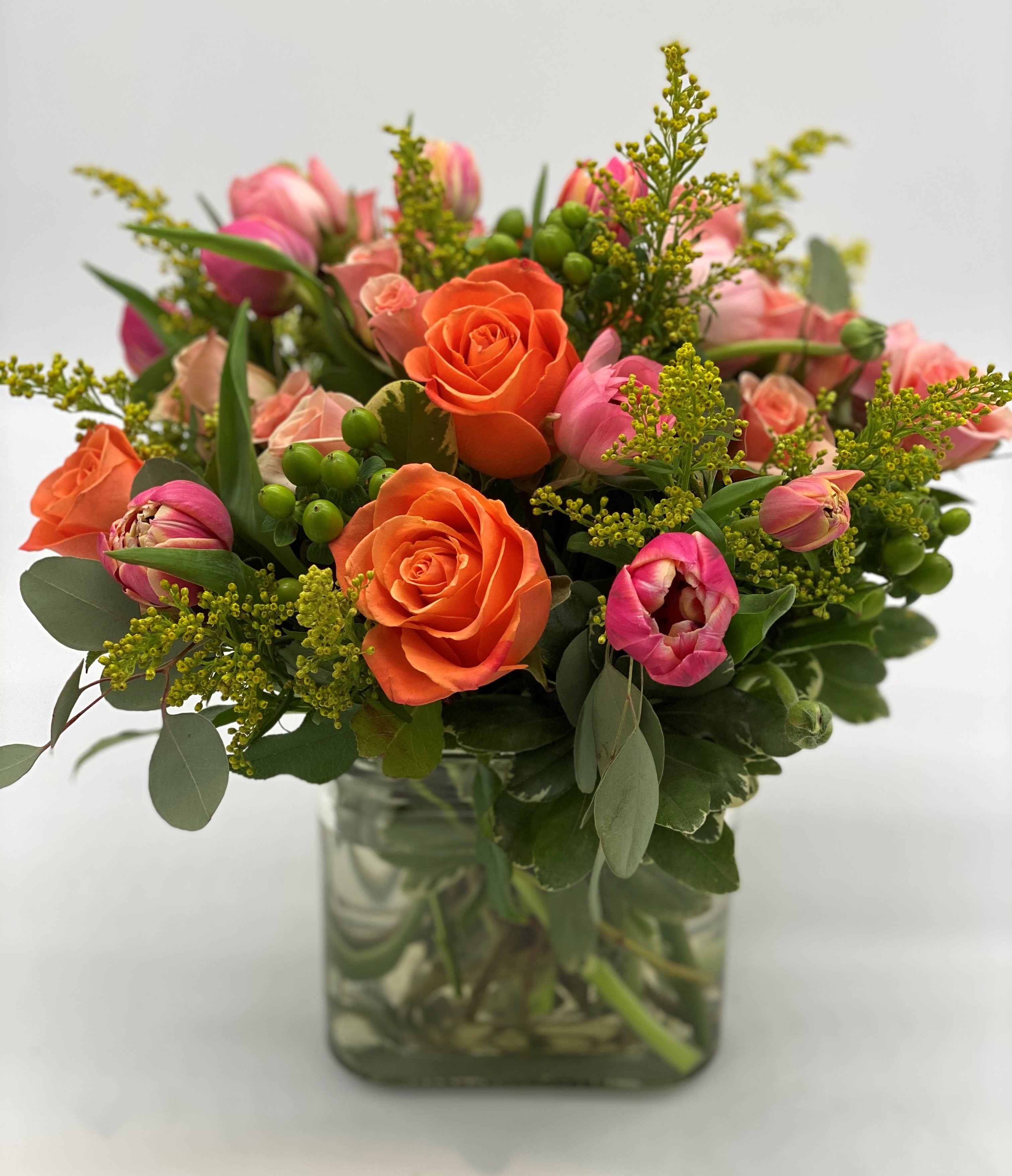 Orange roses and pink tulips in a clear glass vase