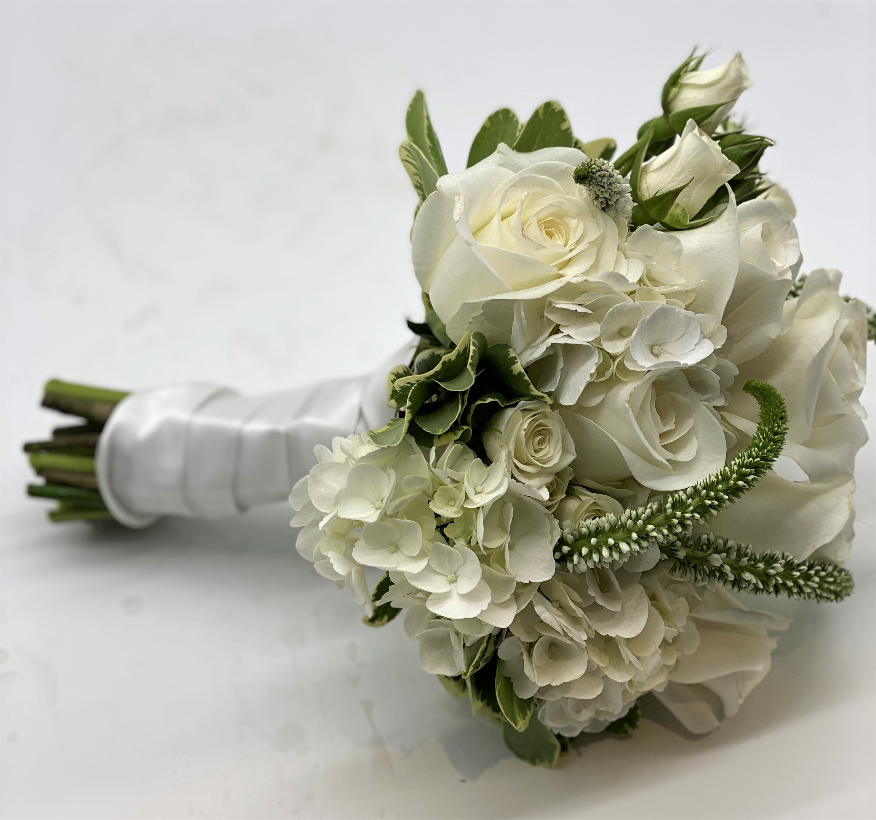 The Classic White Clutch Bouquet - A lush mix of white flowers finished off with a white satin ribbon. 