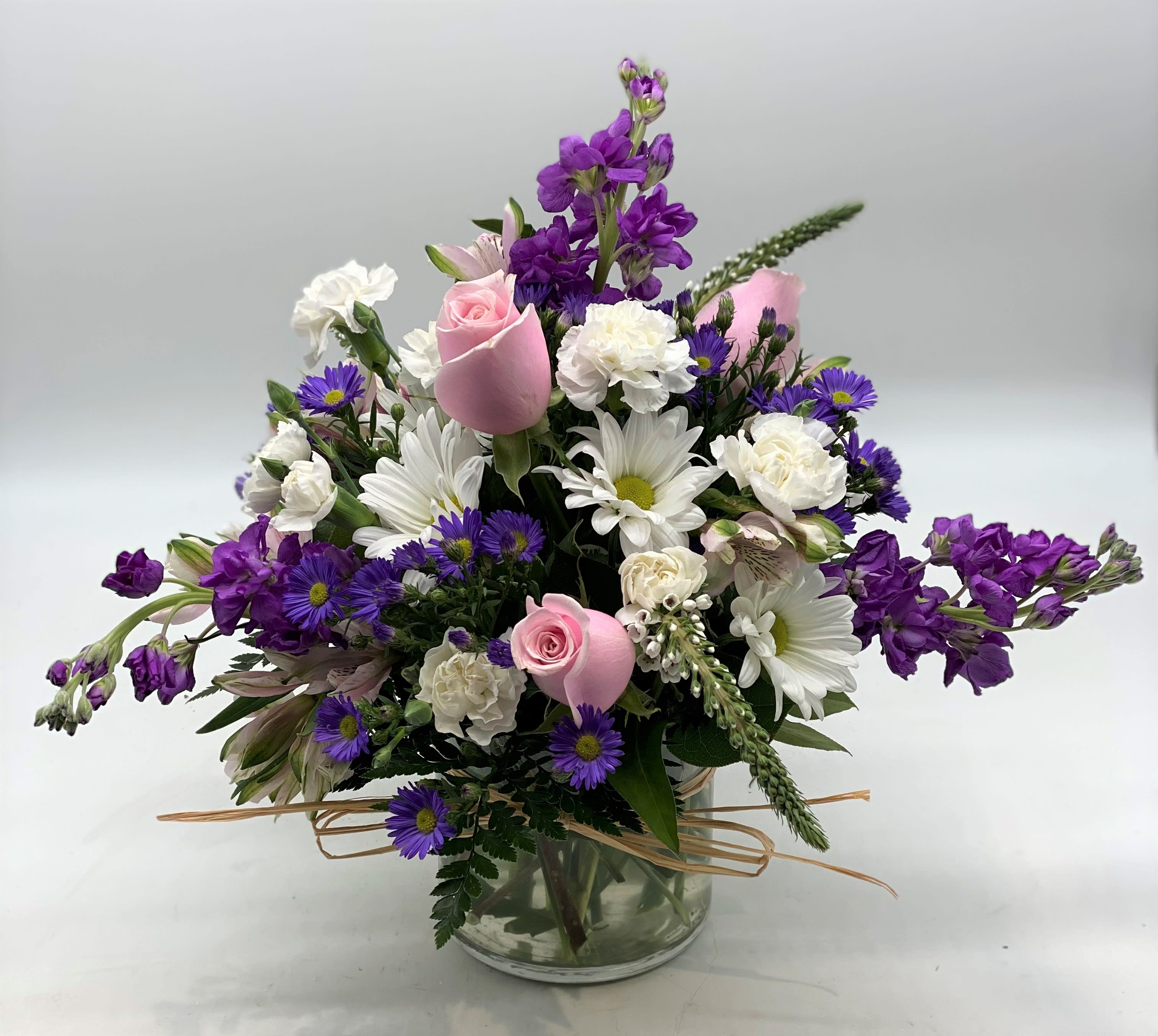 Mixed bouquet of pink roses, white daisies, and purple flowers in a glass vase