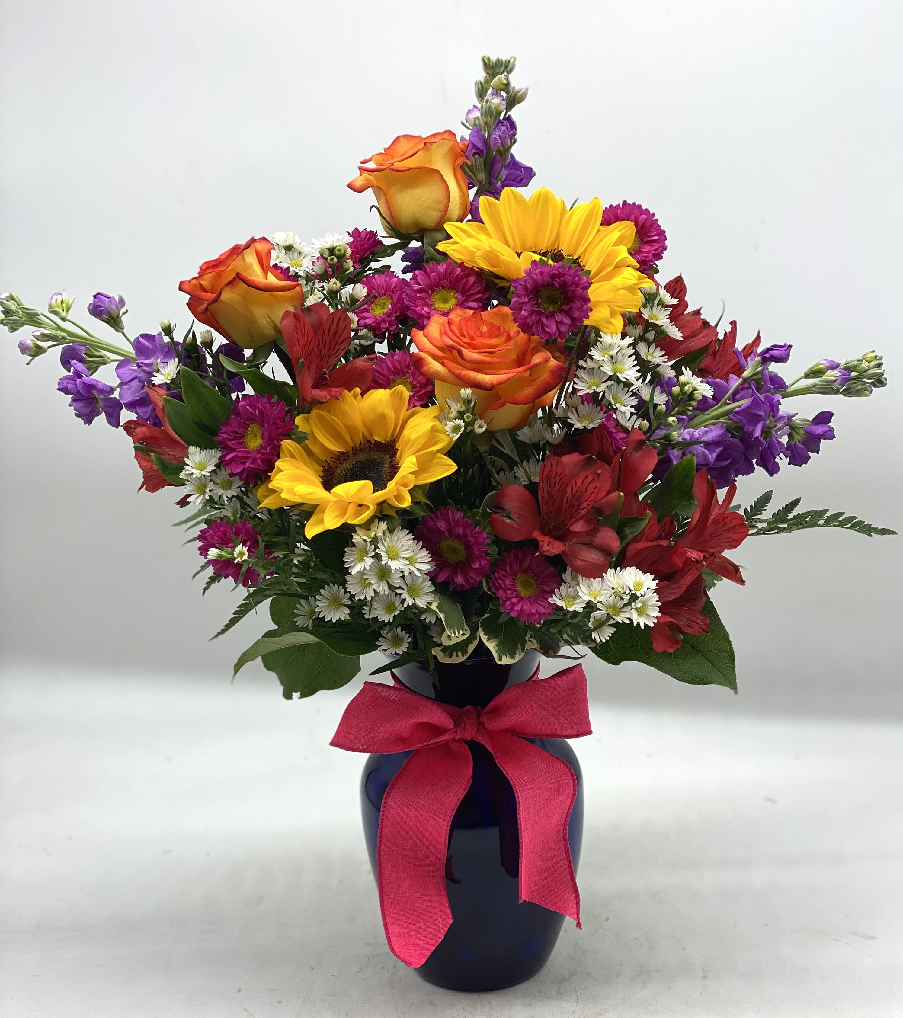 Colorful bouquet with sunflowers, roses, and daisies in a dark vase