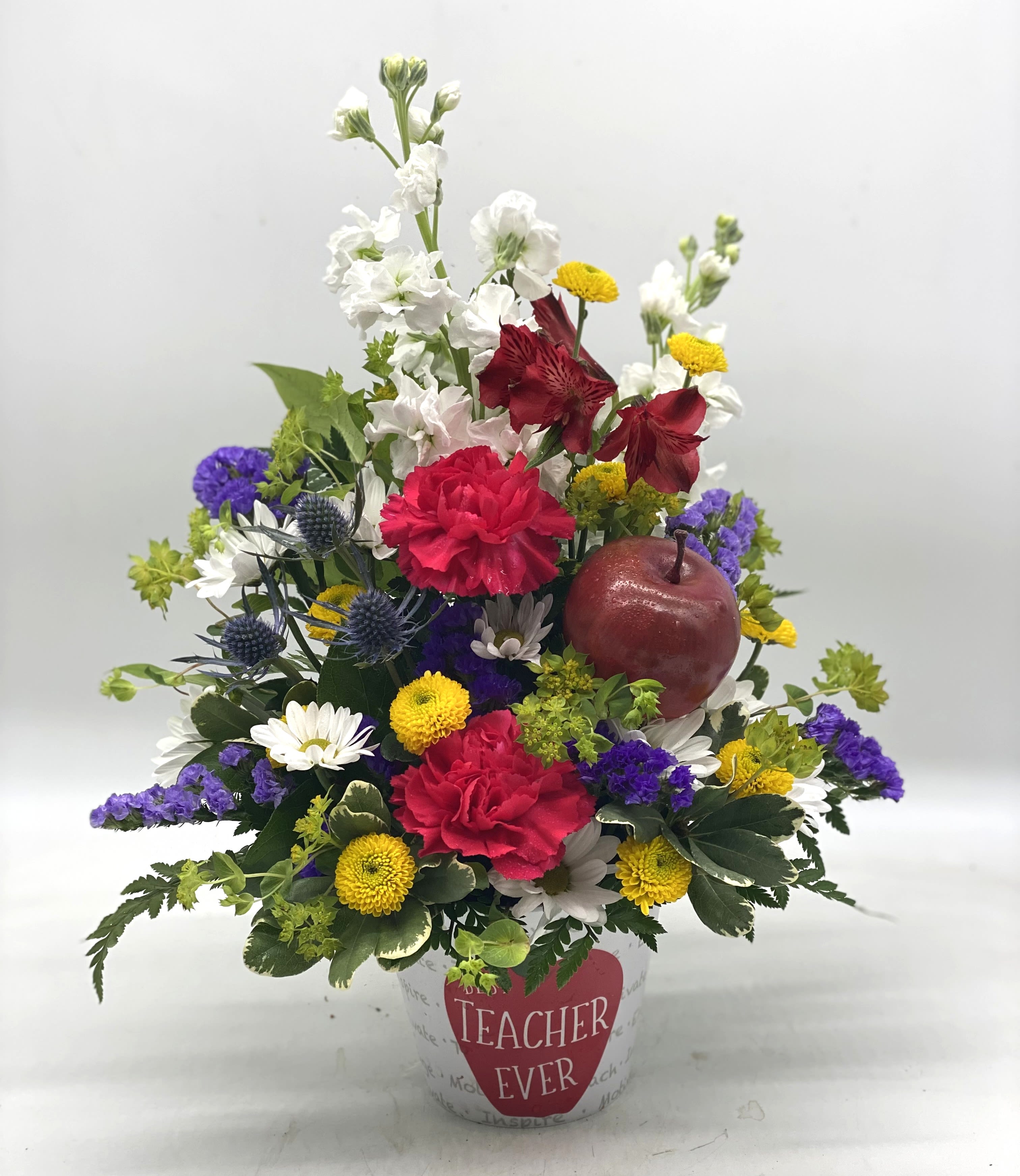 Mixed flower arrangement in a white pot with a "Teacher Ever" label
