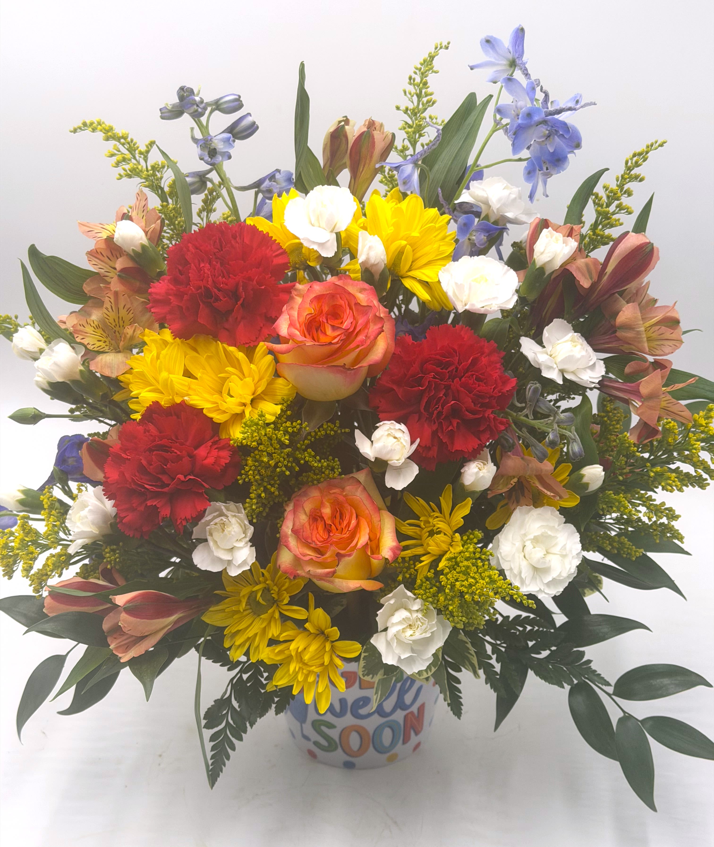 Sunshine &amp; Healing - A vibrant get-well arrangement bursting with cheerful yellow daisies, bi-color roses, red carnations, white mini carnations, blue delphinium and more! Designed in a colorful " Get Well Soon " container, this uplifting bouquet brings warmth, encouragement, and a bright touch of happiness to any recovery space!