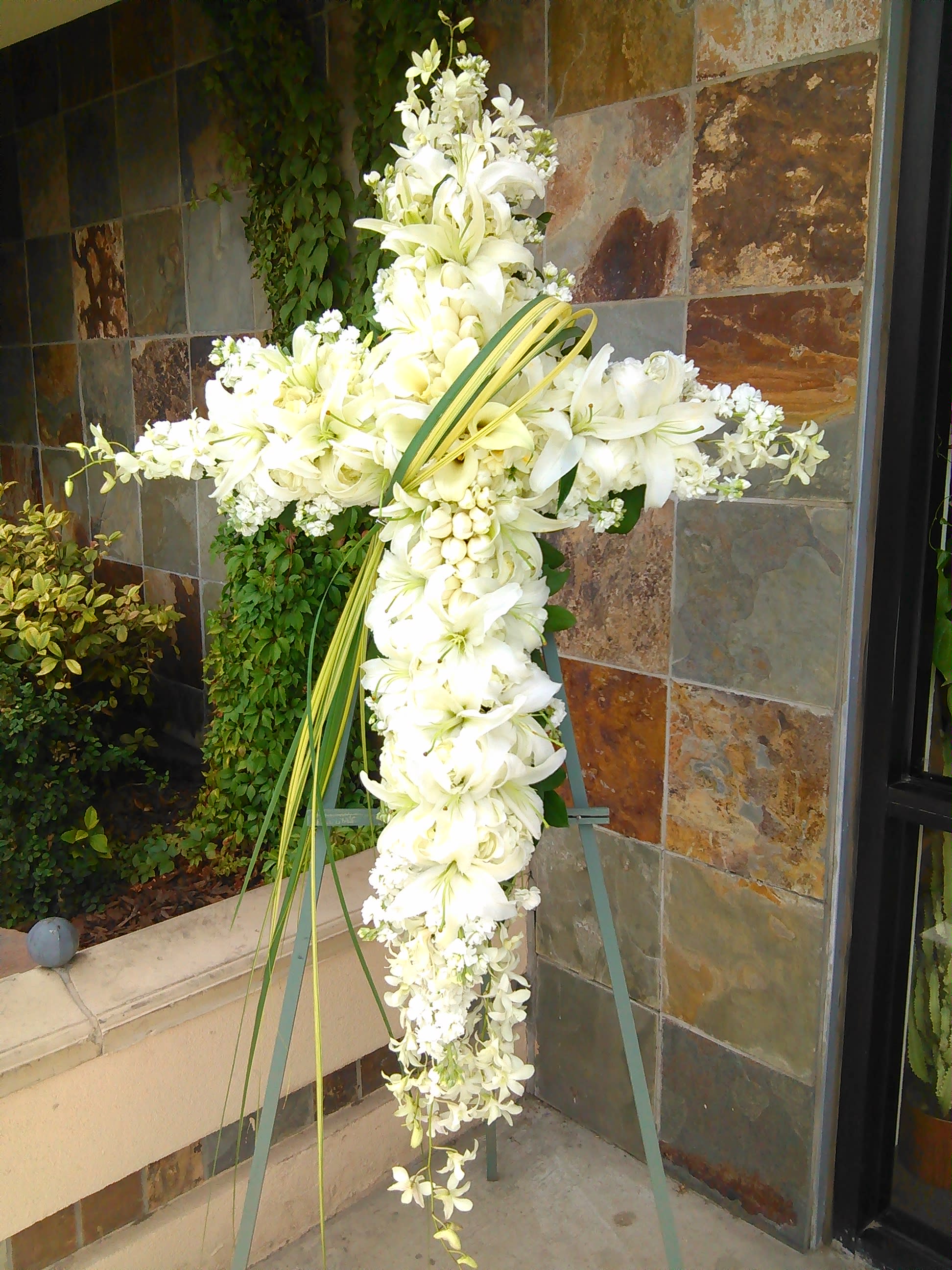 White floral cross on an easel with lilies and orchids