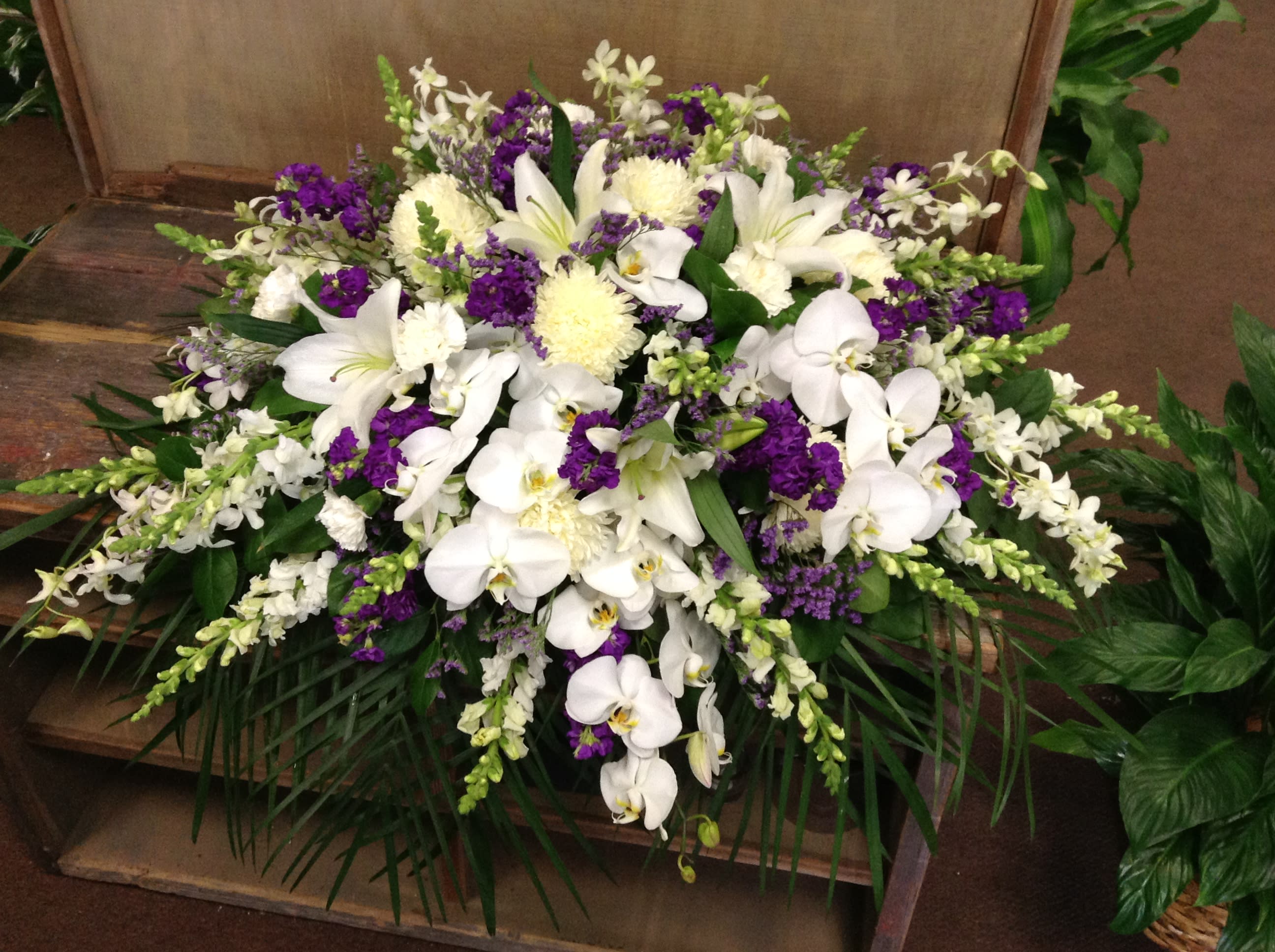 White orchids and lilies arranged with purple flowers in a low spray.