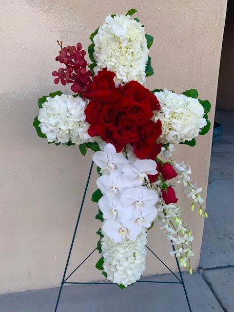 Cross-shaped floral tribute with red roses, white hydrangeas, and white orchids