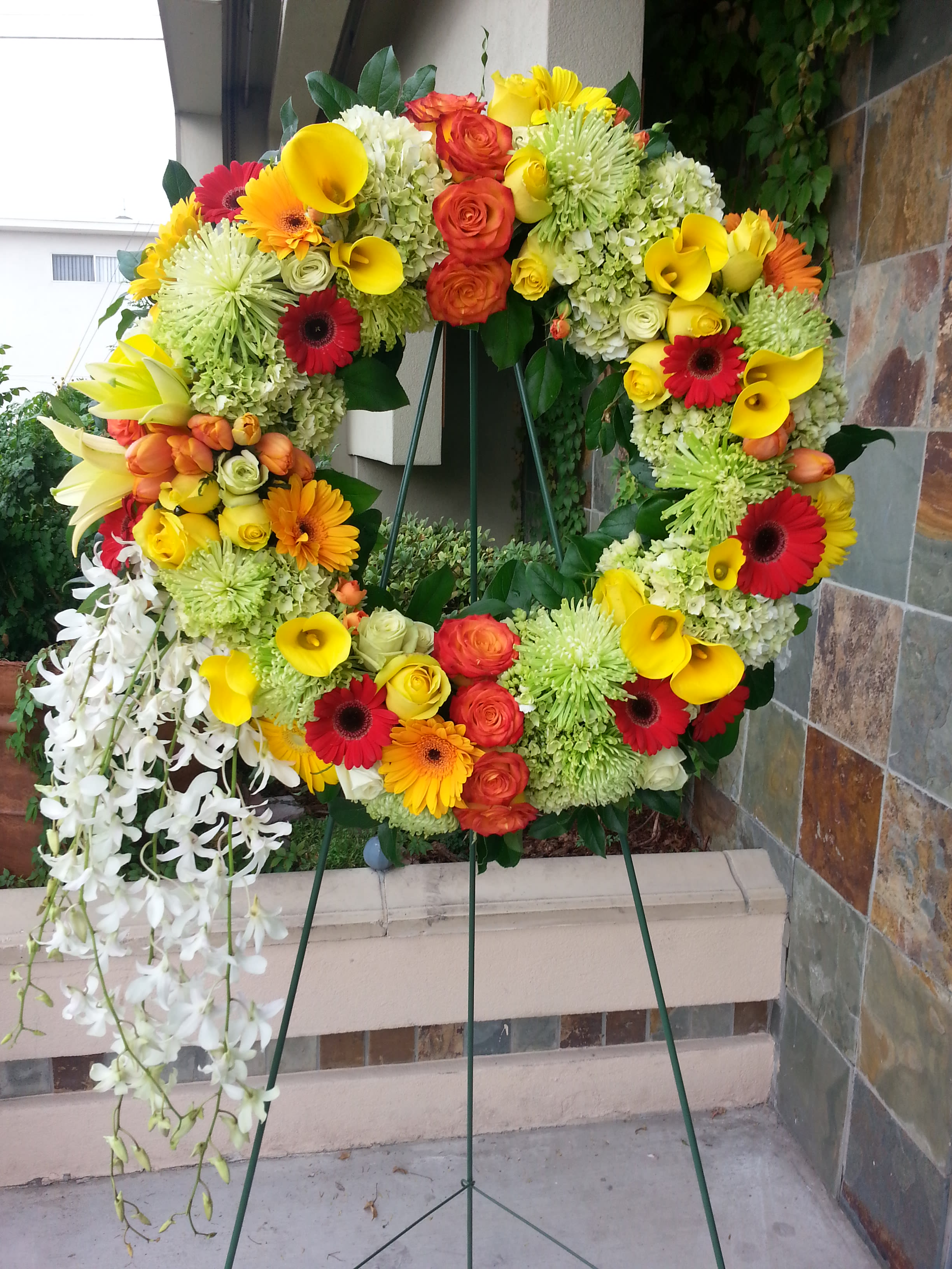 Large floral wreath on an easel with yellow, orange, red, and white blooms