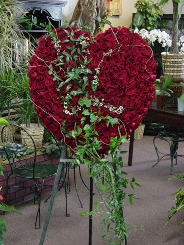 Heart-shaped red rose arrangement on a stand with trailing greenery