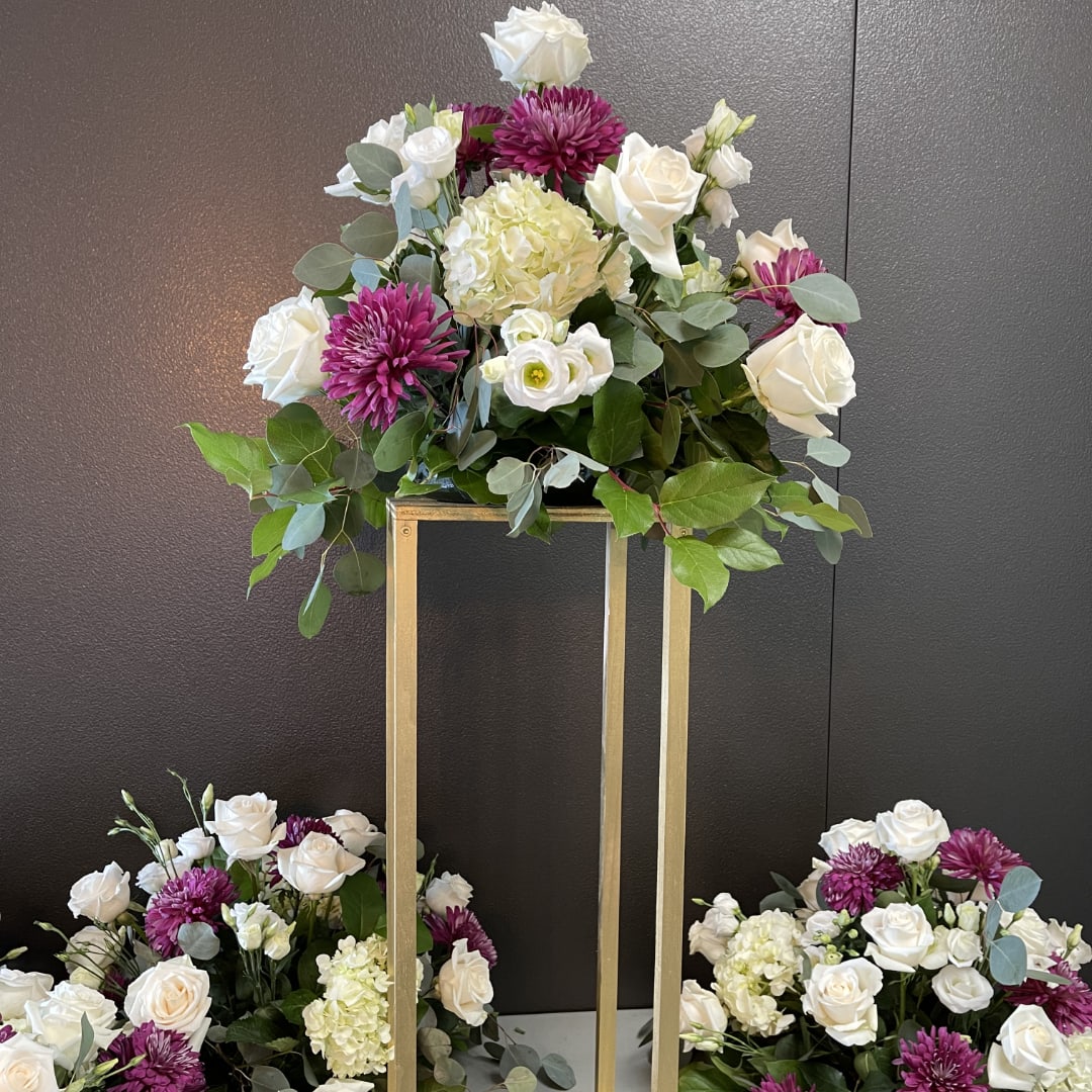 Three floral arrangements with white roses, purple mums, and pale hydrangeas on gold stands