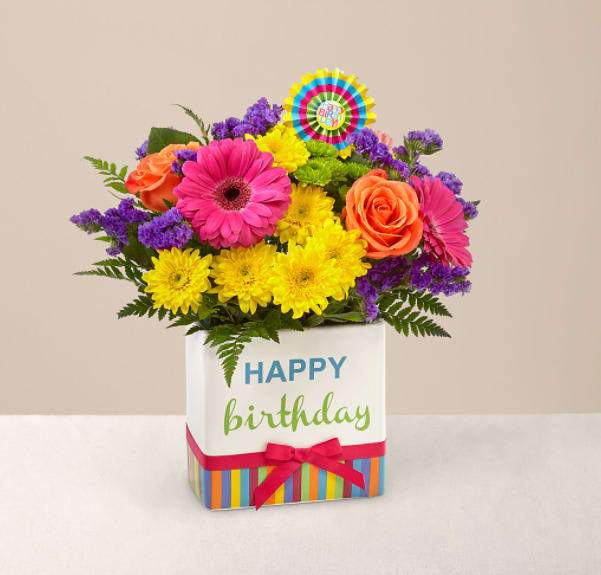 Birthday Brights Bouquet - The Birthday Brights Bouquet is a true celebration of color and life to surprise and delight your special recipient on their big day! Hot pink gerbera daisies and orange roses take center stage surrounded by purple statice, yellow cushion poms, green button poms, and lush greens to create party perfect birthday display. Presented in a modern rectangular ceramic vase with colorful striping at the bottom, "Happy Birthday" lettering at the top, and a bright pink bow at the center, this unforgettable fresh flower arrangement is then accented with a striped happy birthday pick to create a fun and festive gift.