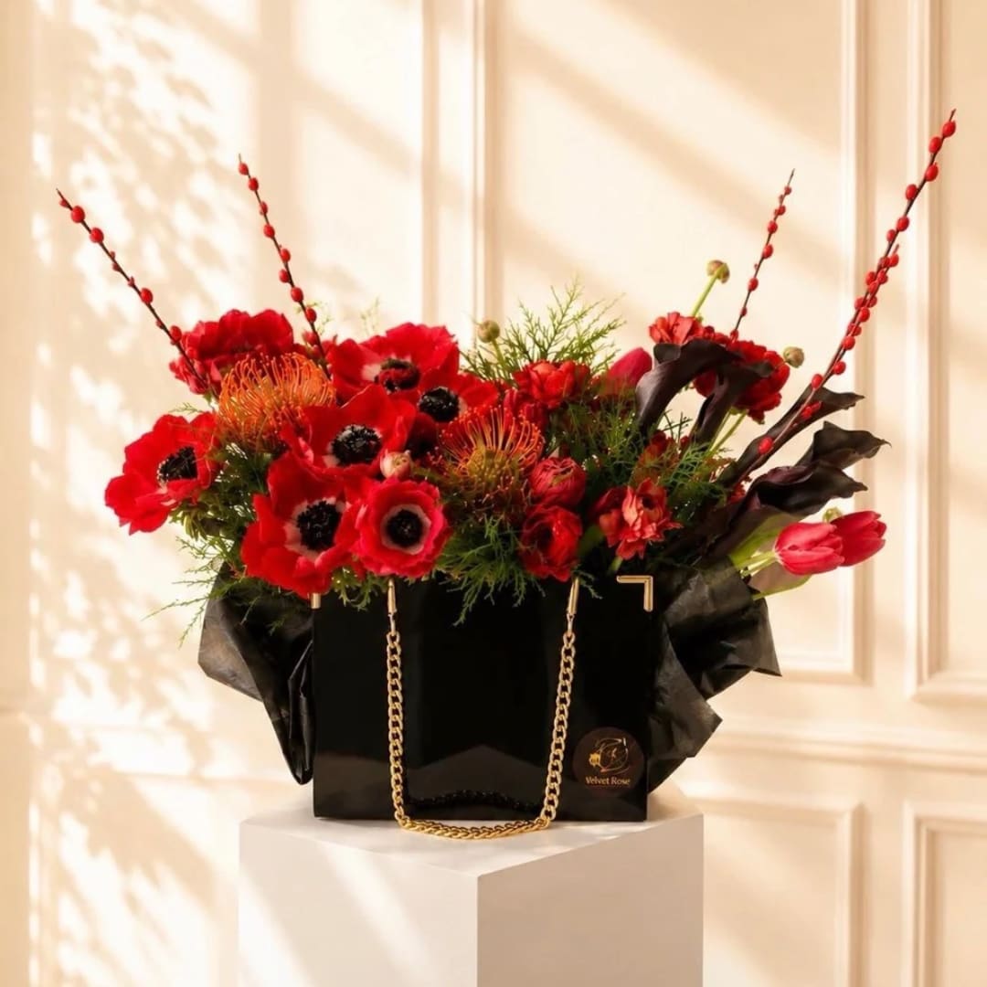 Red floral arrangement in a black gift bag with gold chain handles
