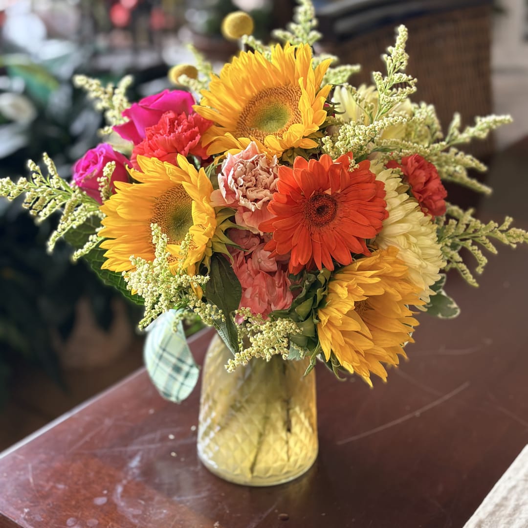 Mixed bouquet of sunflowers, roses, and gerbera daisies in a gold vase