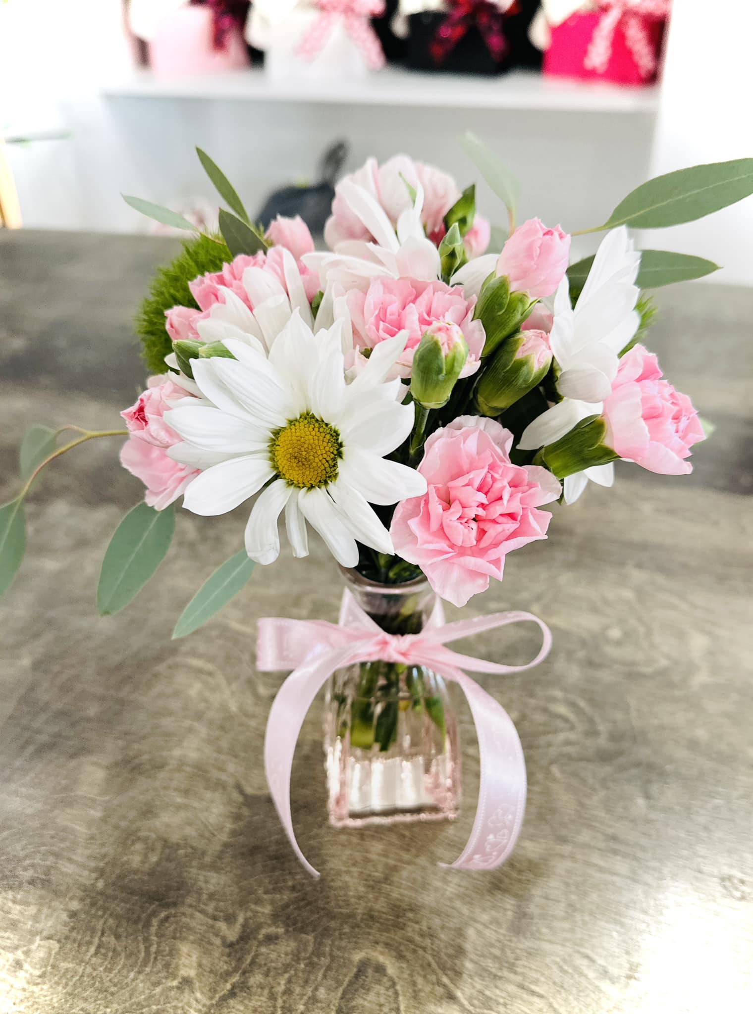 Pink carnations and white daisies in a clear glass vase with a pink ribbon