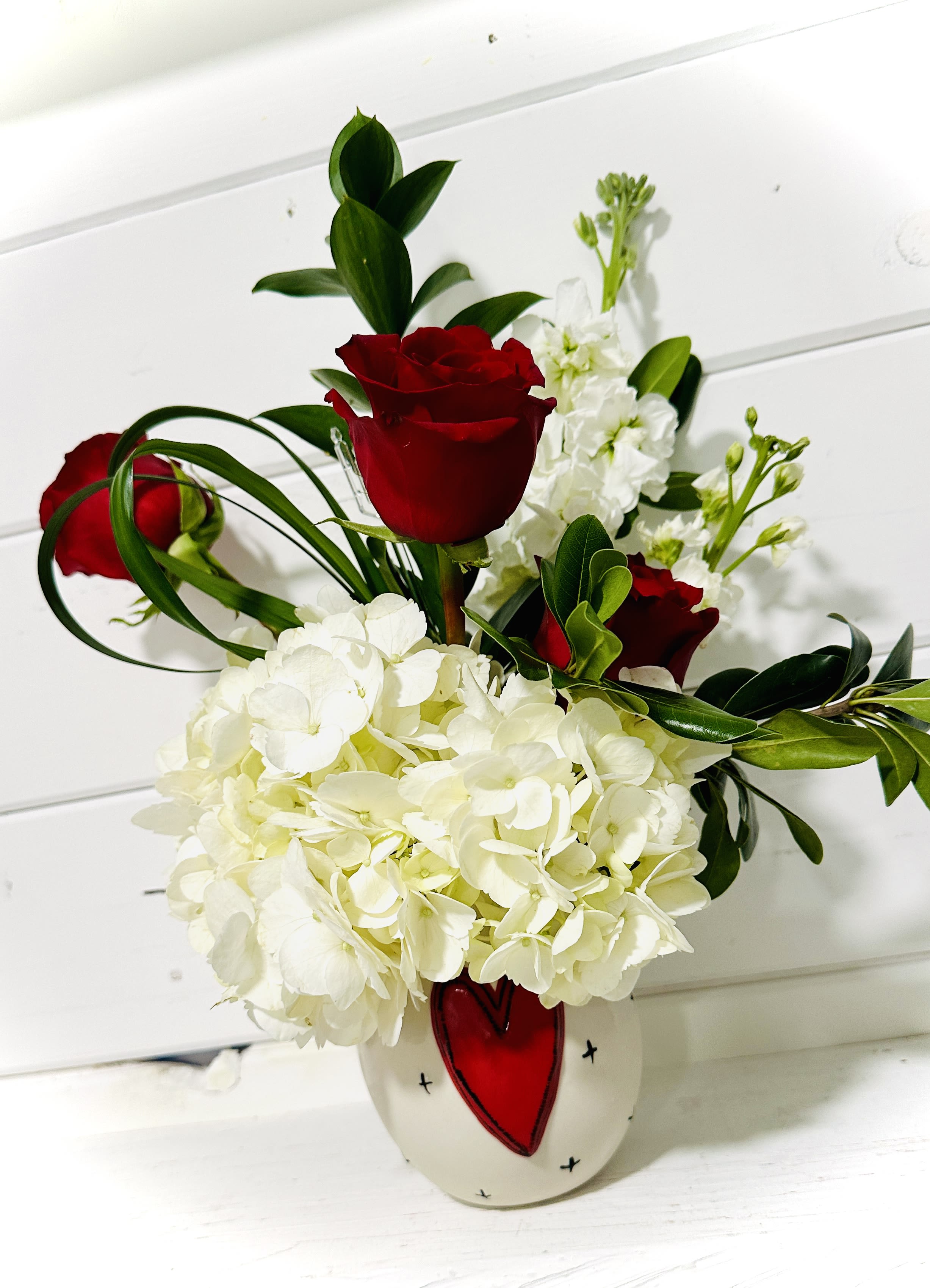 Red roses and white hydrangeas in a white vase with a red heart