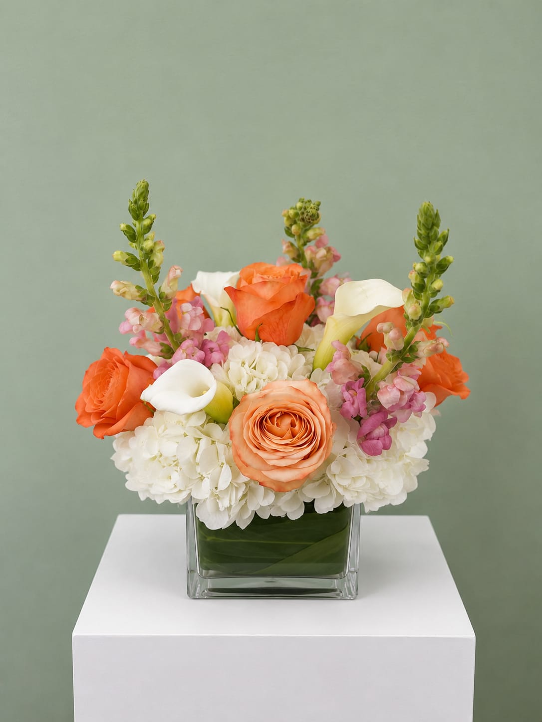 Orange roses and white calla lilies in a square glass vase