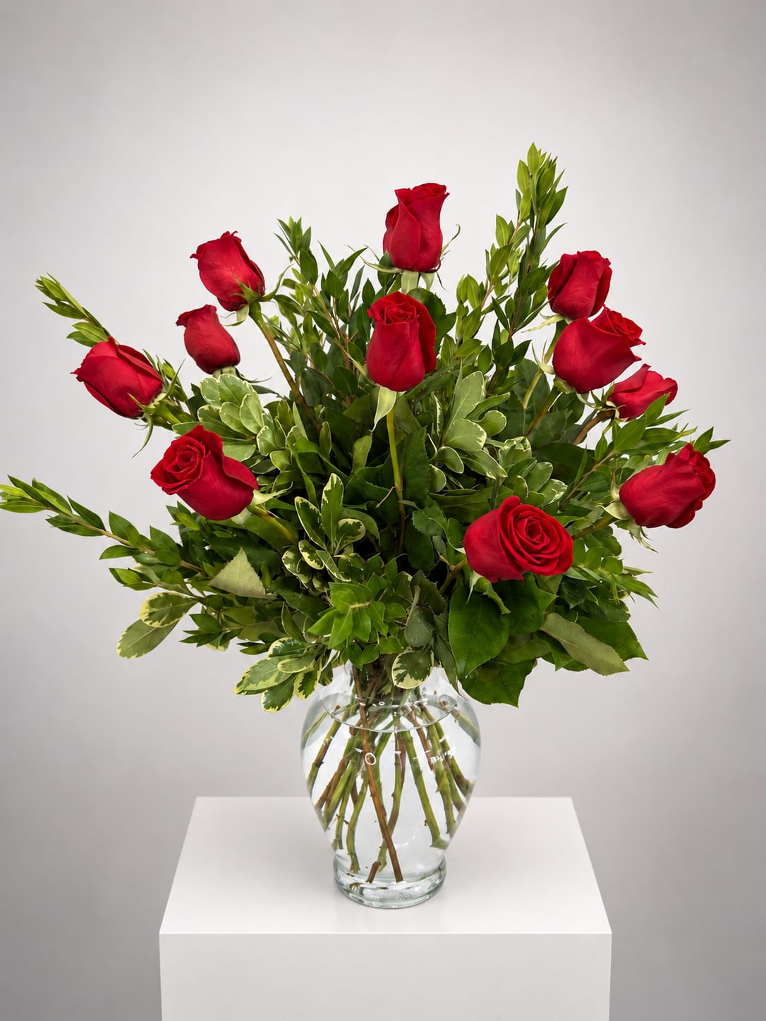 Red roses arranged in a clear glass vase with mixed greenery