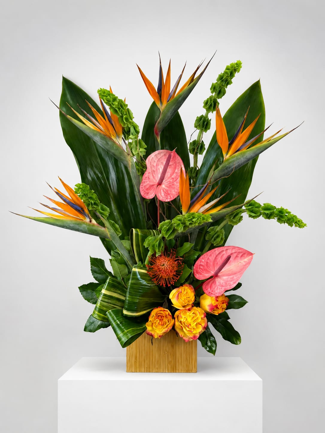 Tropical floral arrangement with pink anthuriums and bird of paradise in a wooden vase