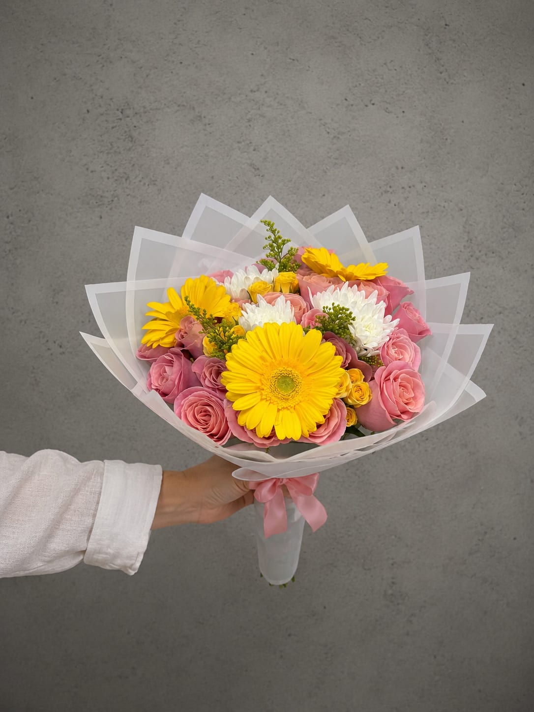 Sunlit Wrap - Sunlit Wrap is a bright, hand-tied bouquet featuring vibrant yellow gerbera daisies, premium pink roses, white chrysanthemums, spray roses, and fresh seasonal greenery. Wrapped in elegant blush paper, this cheerful bouquet is perfect for birthdays, anniversaries, celebrations, thank you gifts, get well wishes, or simply to brighten someone's day.  Each bouquet is handcrafted by the designers at All Occasions Florist using the freshest flowers available. While flower varieties may vary slightly based on seasonal availability, our designers will always create a bouquet with the same beautiful color palette and premium style. We proudly offer same-day flower delivery throughout Dallas and surrounding areas.  Important: This is a wrapped bouquet only and does not include a vase. The recipient must unwrap the bouquet, trim the stems, and place the flowers in fresh water immediately upon delivery. Flowers left without water may wilt and have a significantly reduced vase life. Because proper care is the recipient's responsibility, wrapped bouquets are not eligible for refunds or replacements 