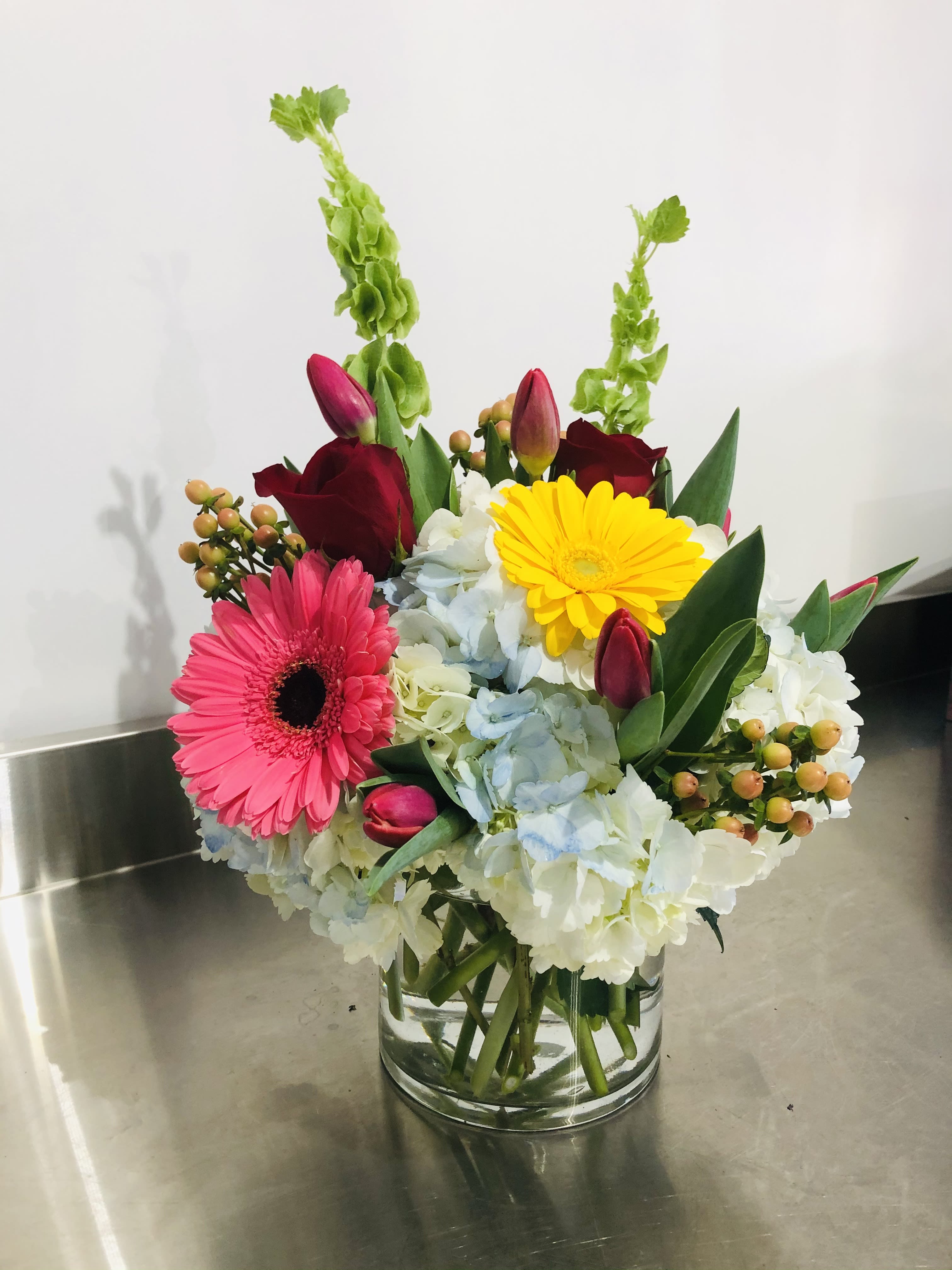 Eye catcher - Beautiful design filled with blue and white hydrangea, tulips, gerbera daisies, bells of Ireland, hypericum berries and roses. It will be sure to catch their eye. 