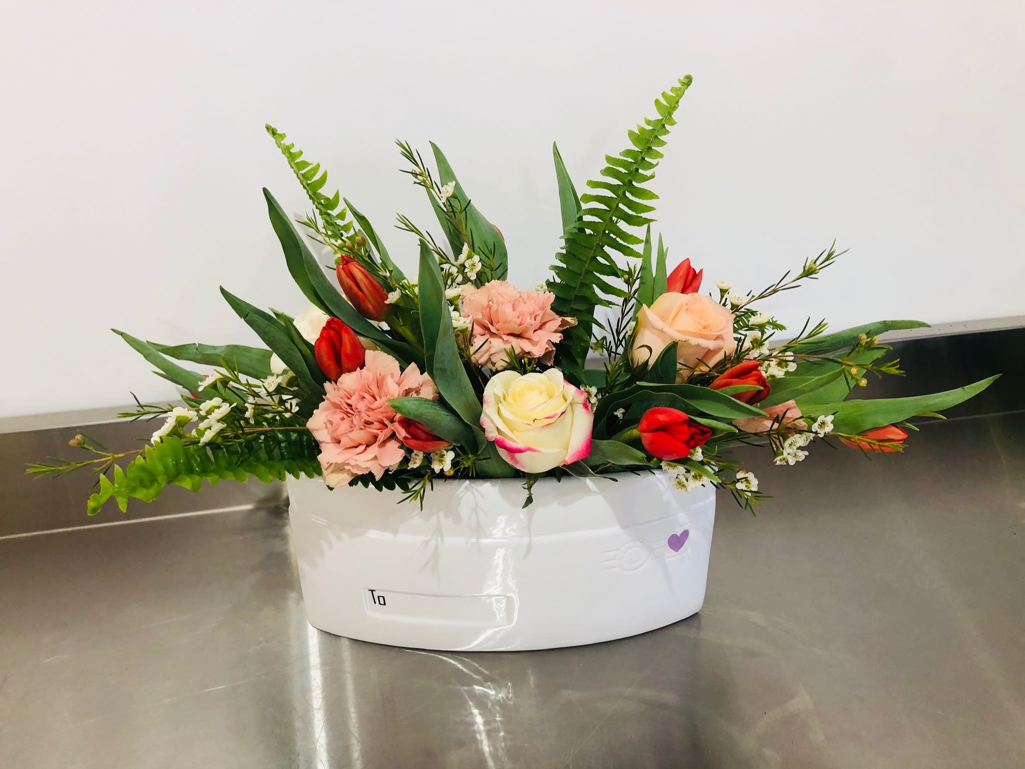 Mixed bouquet of roses, tulips, and carnations in a white container