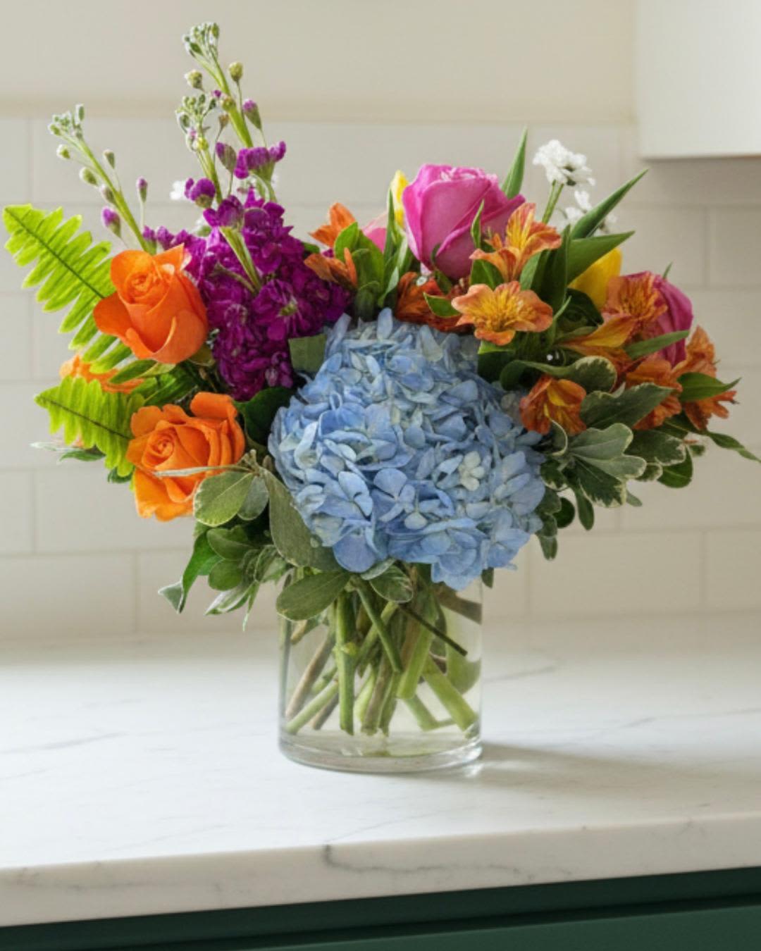 Colorful bouquet with blue hydrangea, orange and pink roses in a glass vase