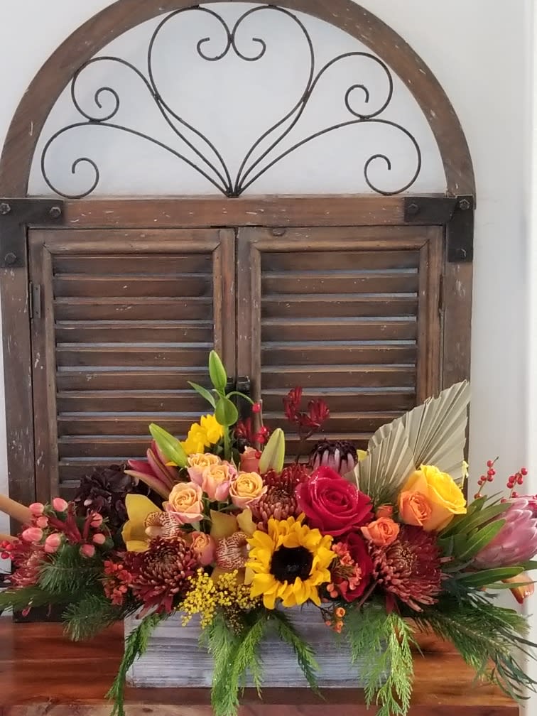 Colorful mixed flower arrangement in a rectangular container with a rustic window backdrop