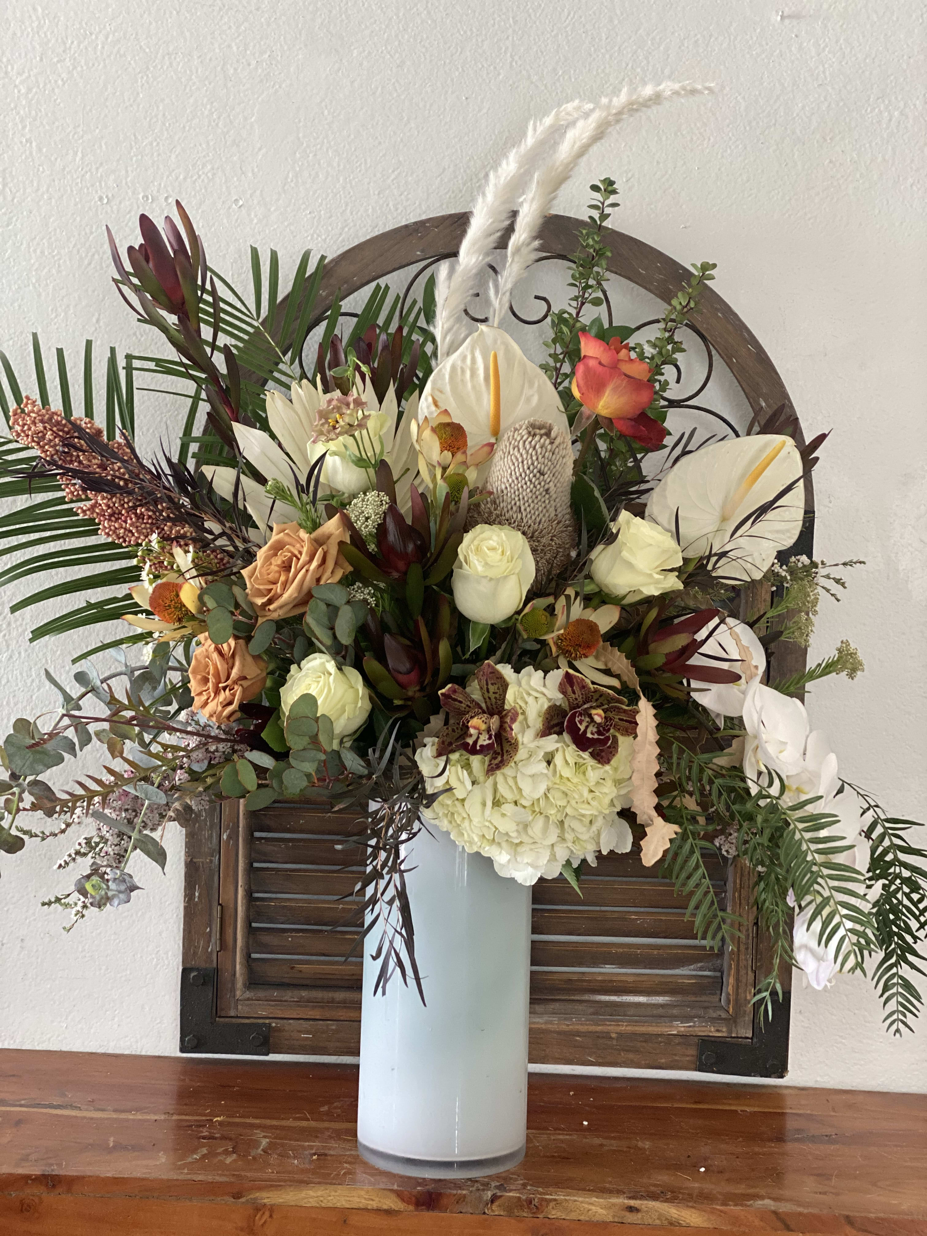 Large mixed floral arrangement in a tall white vase with white anthuriums and roses