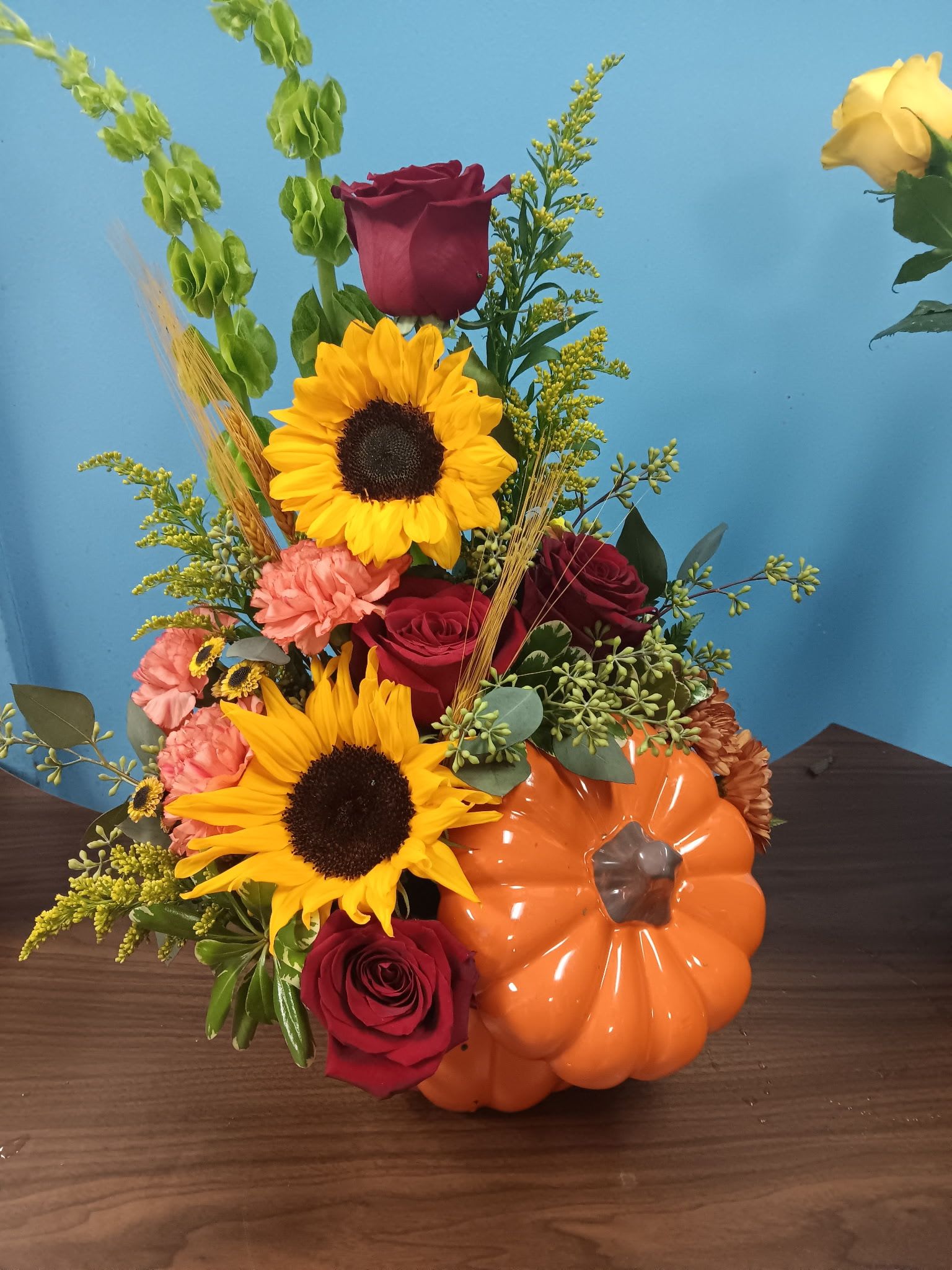 Autumn bouquet with sunflowers, red roses, and a pumpkin container