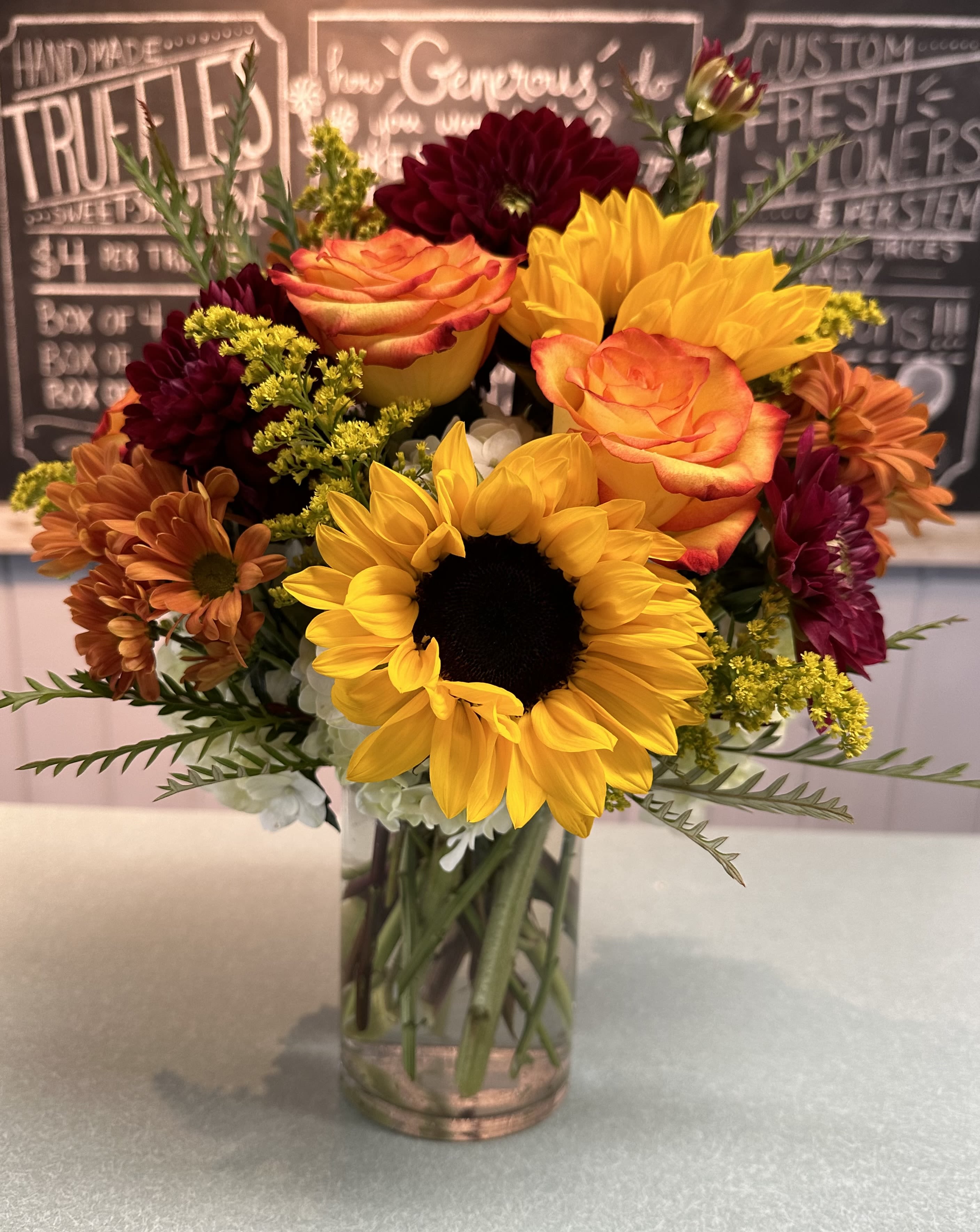 Fall Sunset - Sunflowers, high and magic roses, white hydrangea, butterscotch daisy's, red cremones, solidago and grevillea in a clear glass cylinder