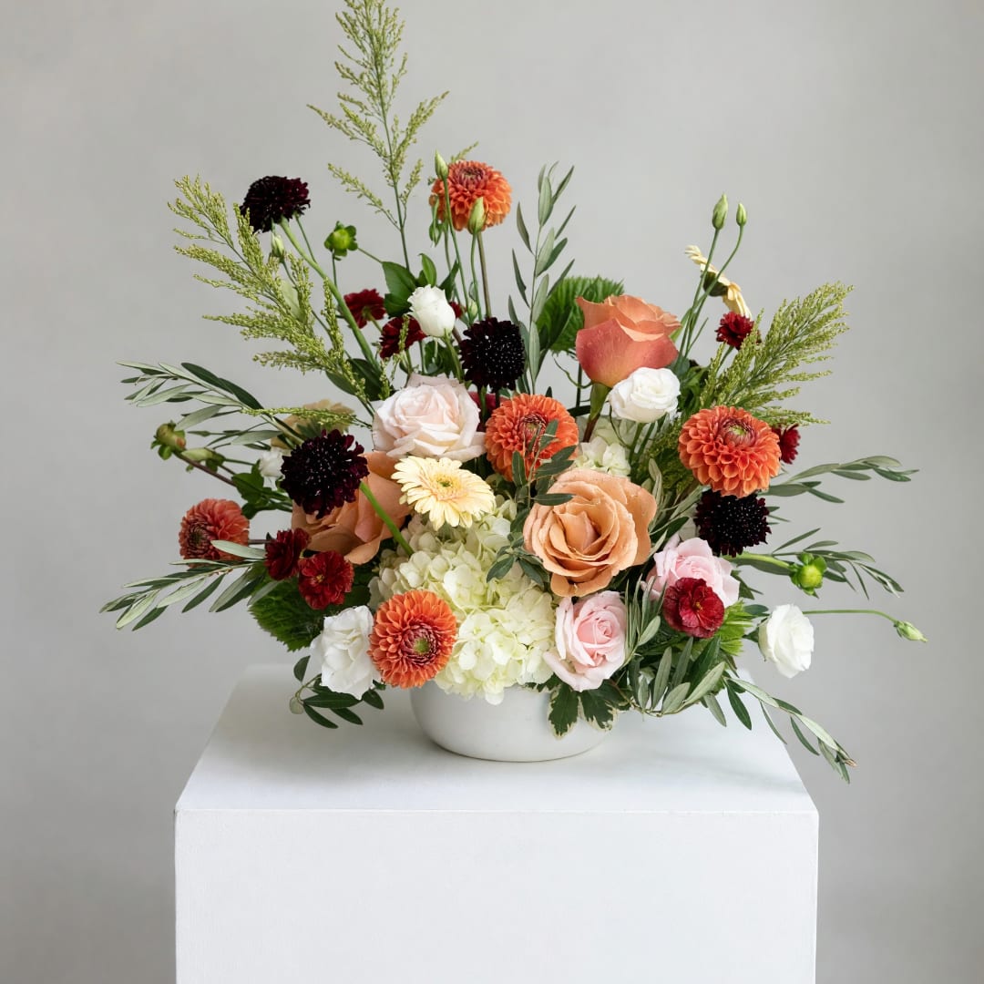 Mixed bouquet in a white bowl vase with peach, white, orange, and burgundy flowers