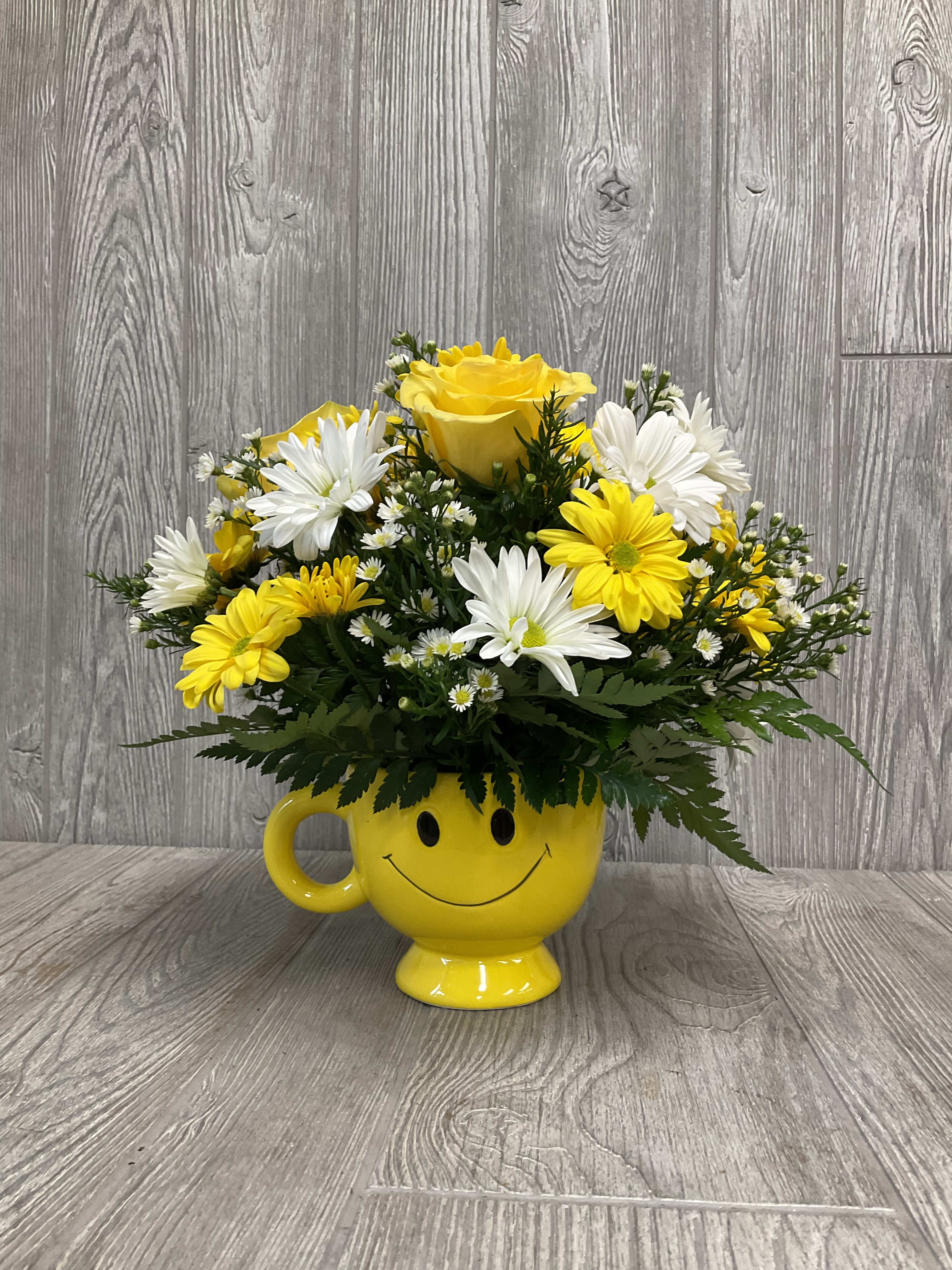 Yellow and white flowers arranged in a yellow smiley-face mug