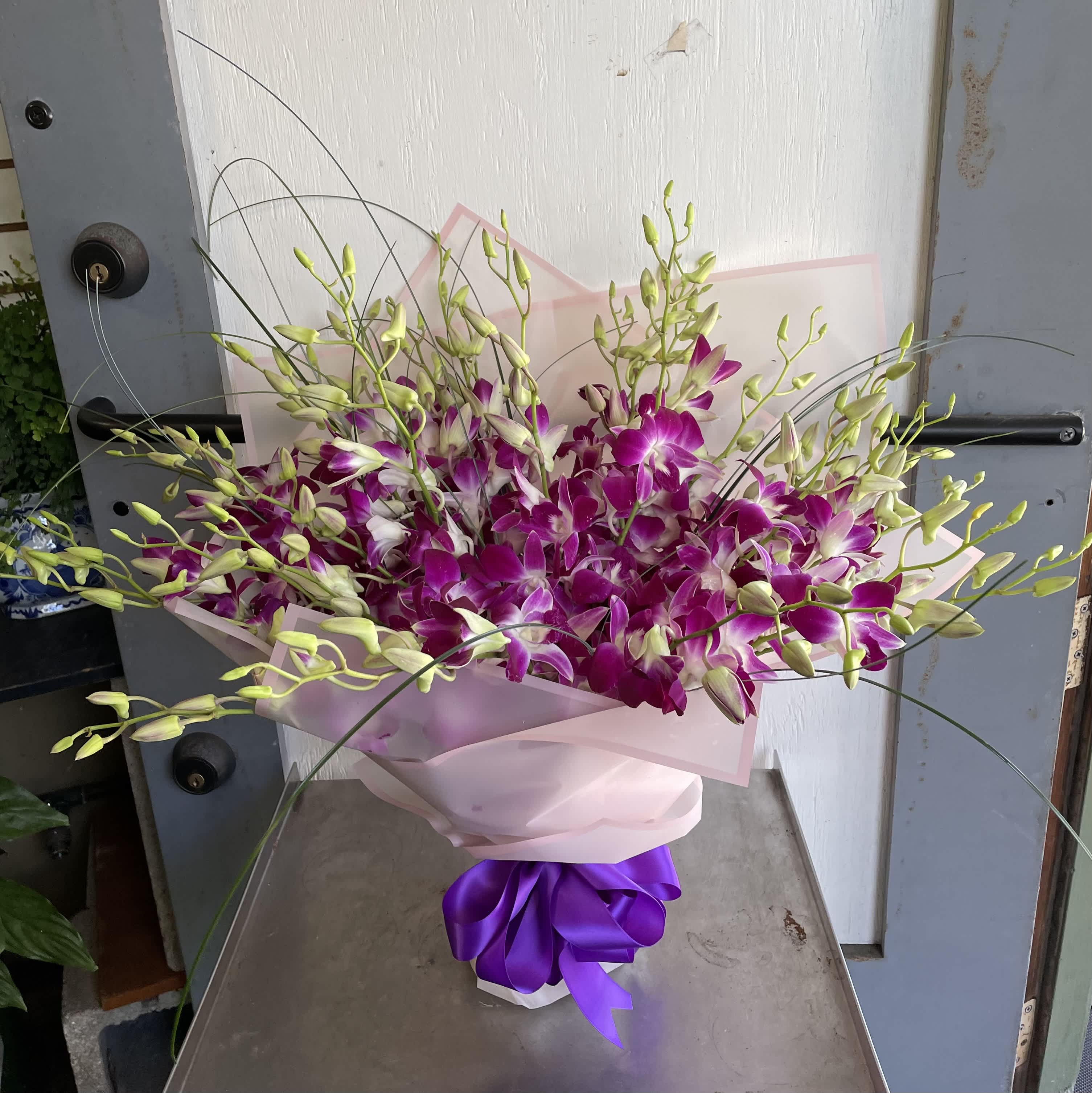 Bouquet of purple and white orchids wrapped in pink paper with a purple ribbon