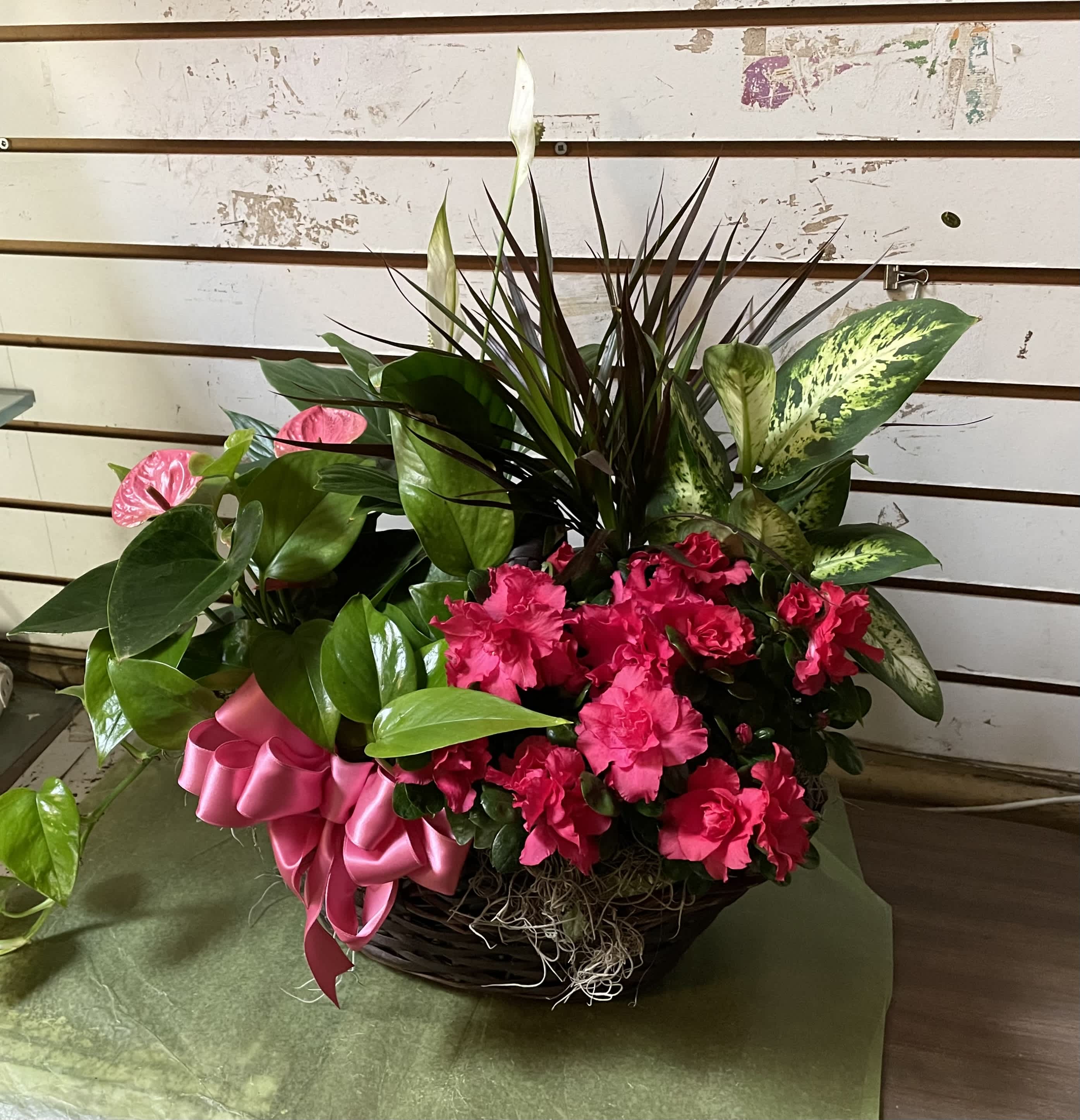 Pink flowers and mixed tropical foliage in a basket with a pink ribbon