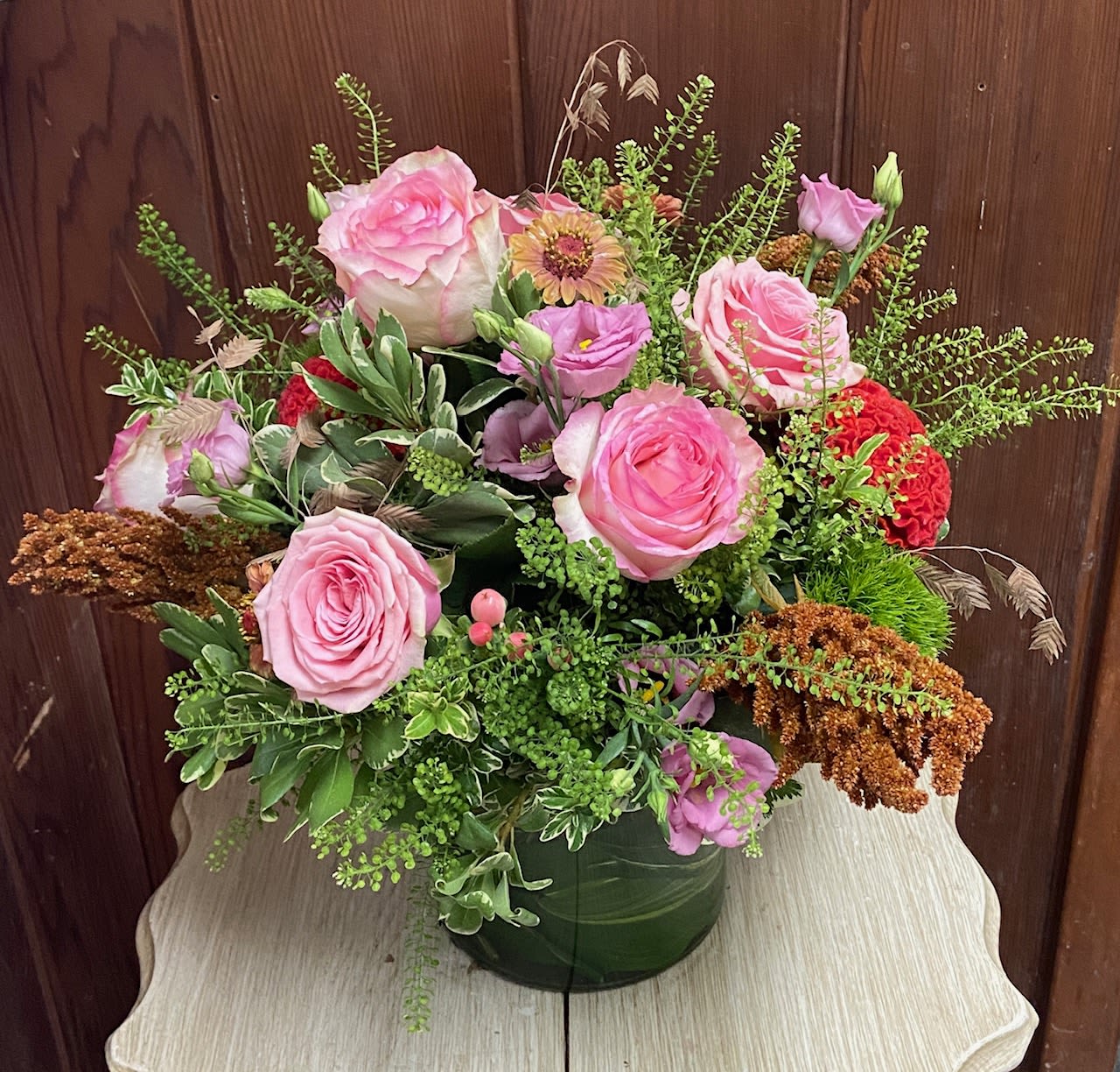 Mixed arrangement of pink roses and purple blooms in a leaf-wrapped glass vase