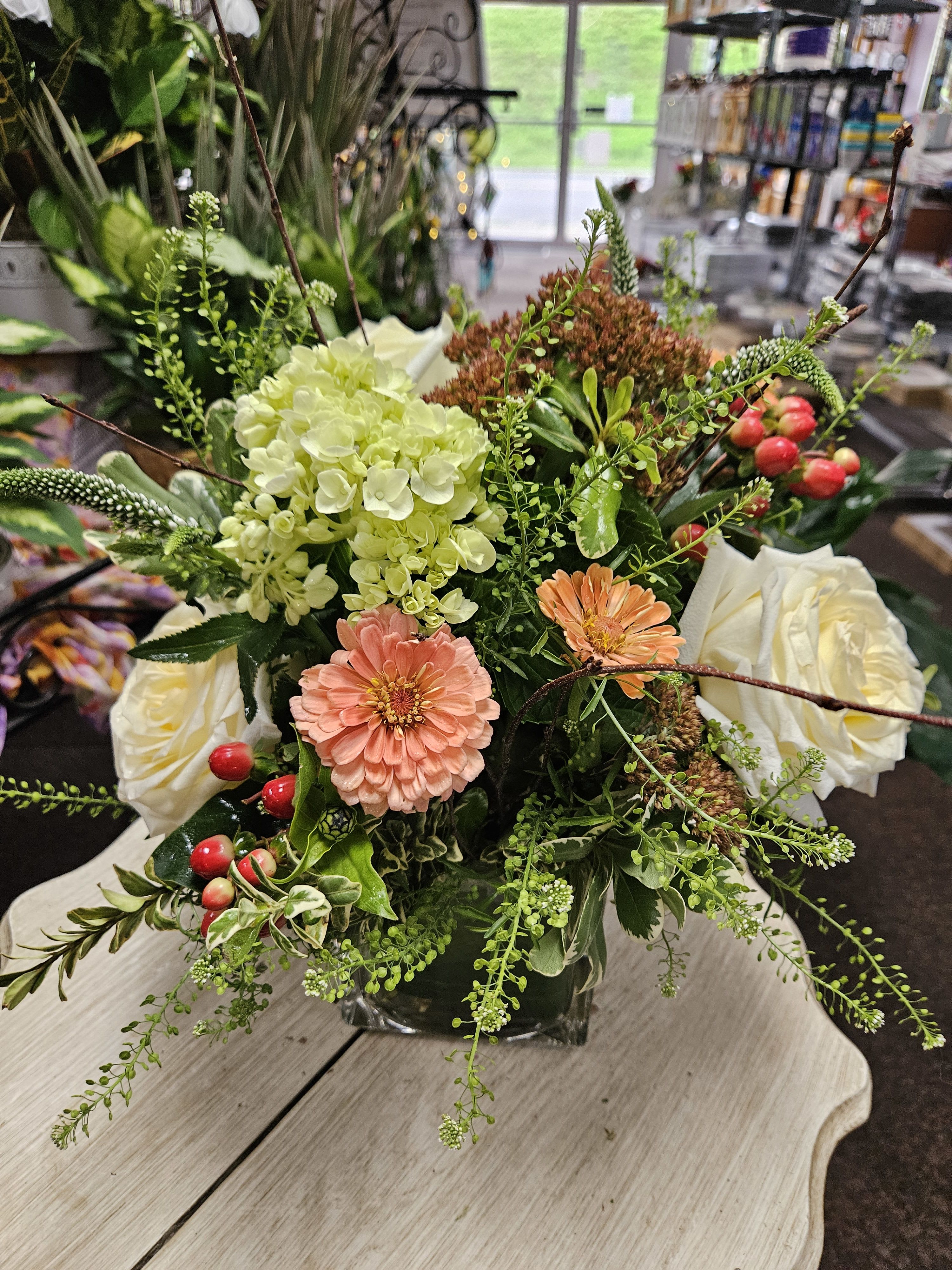 Low mixed arrangement with peach blooms, white roses, hydrangea, and berries in a square glass vase