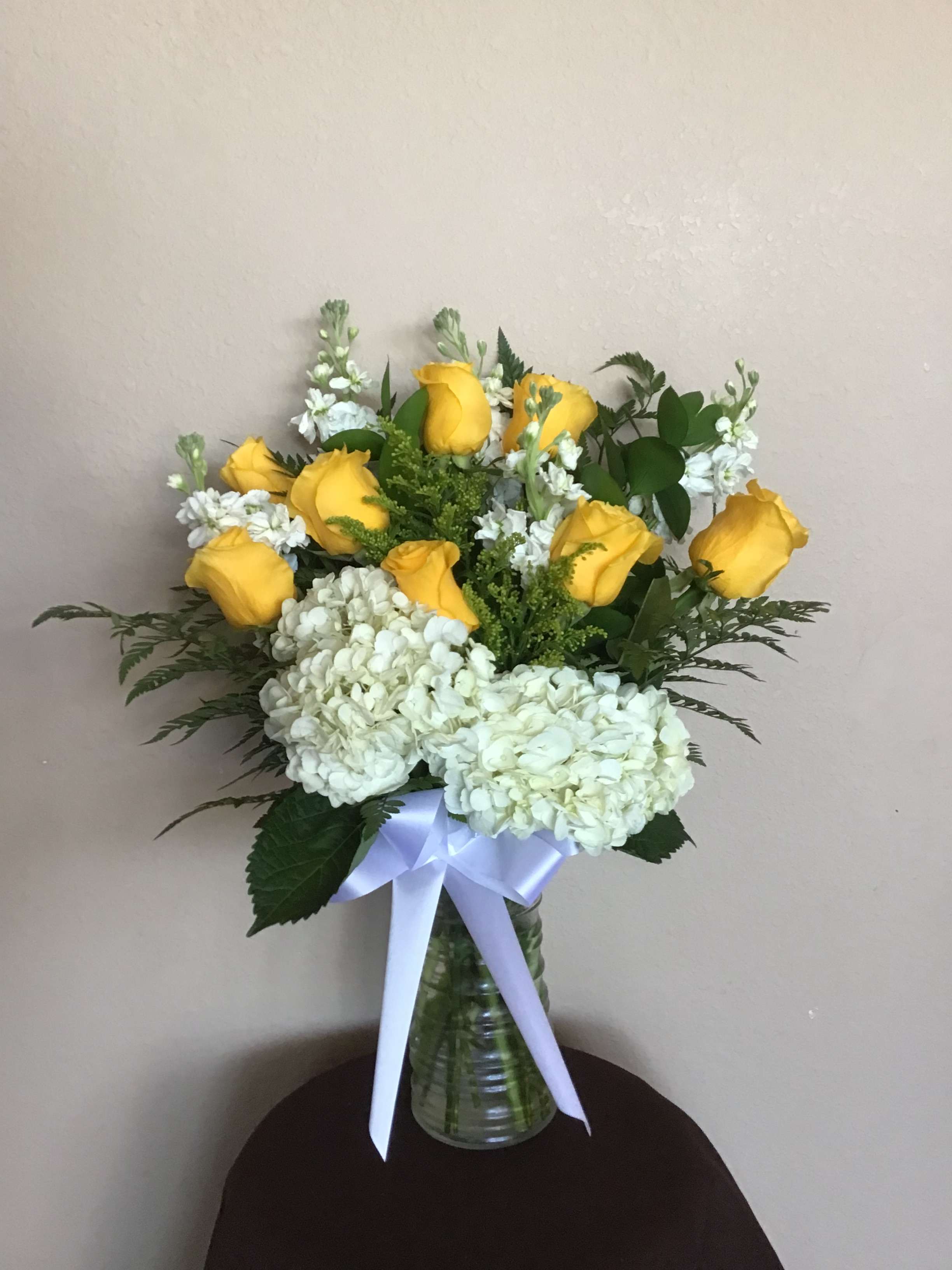Yellow roses and white hydrangeas in a glass vase with a white ribbon