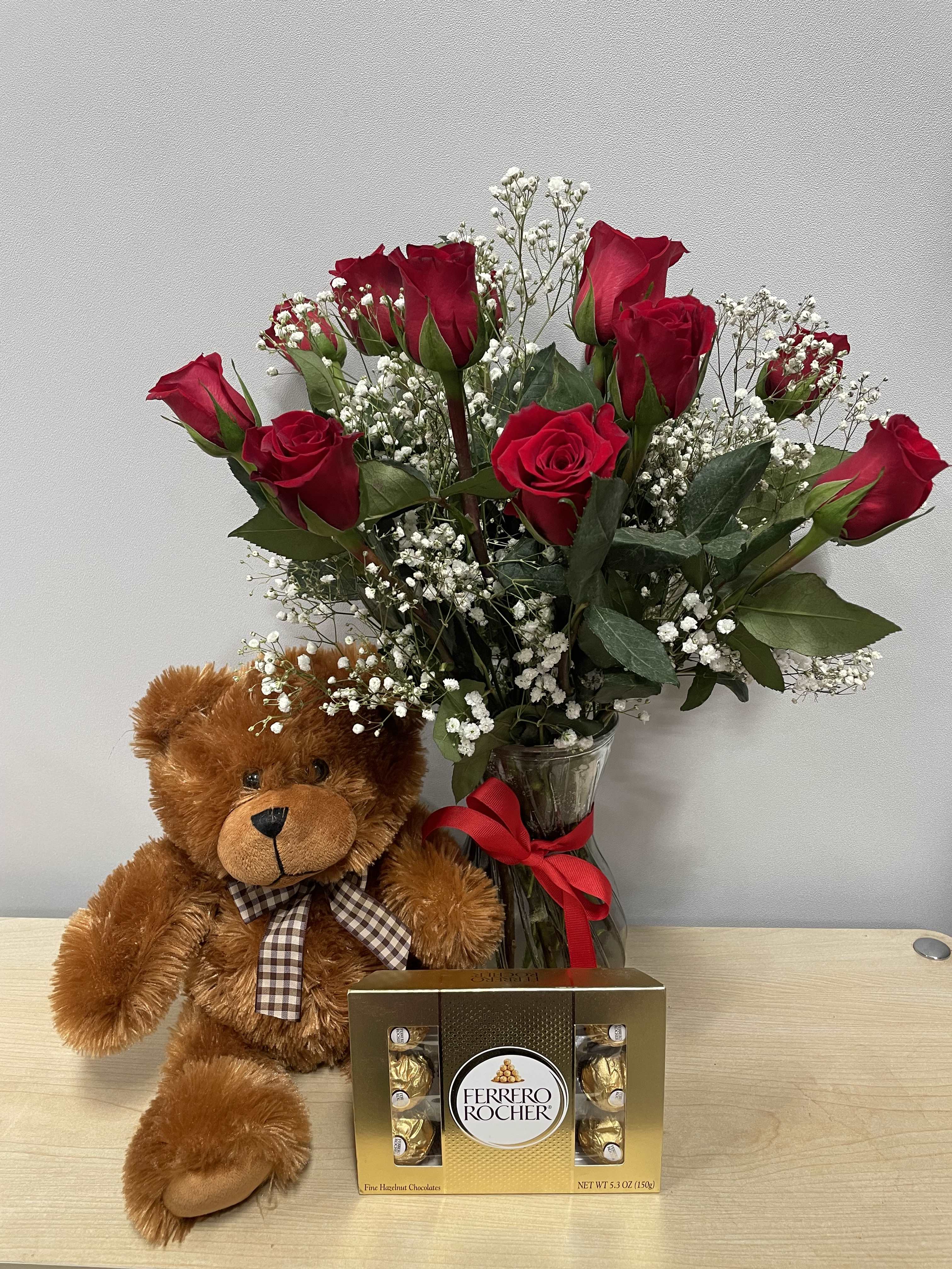 Red roses in a glass vase with a teddy bear and chocolate box