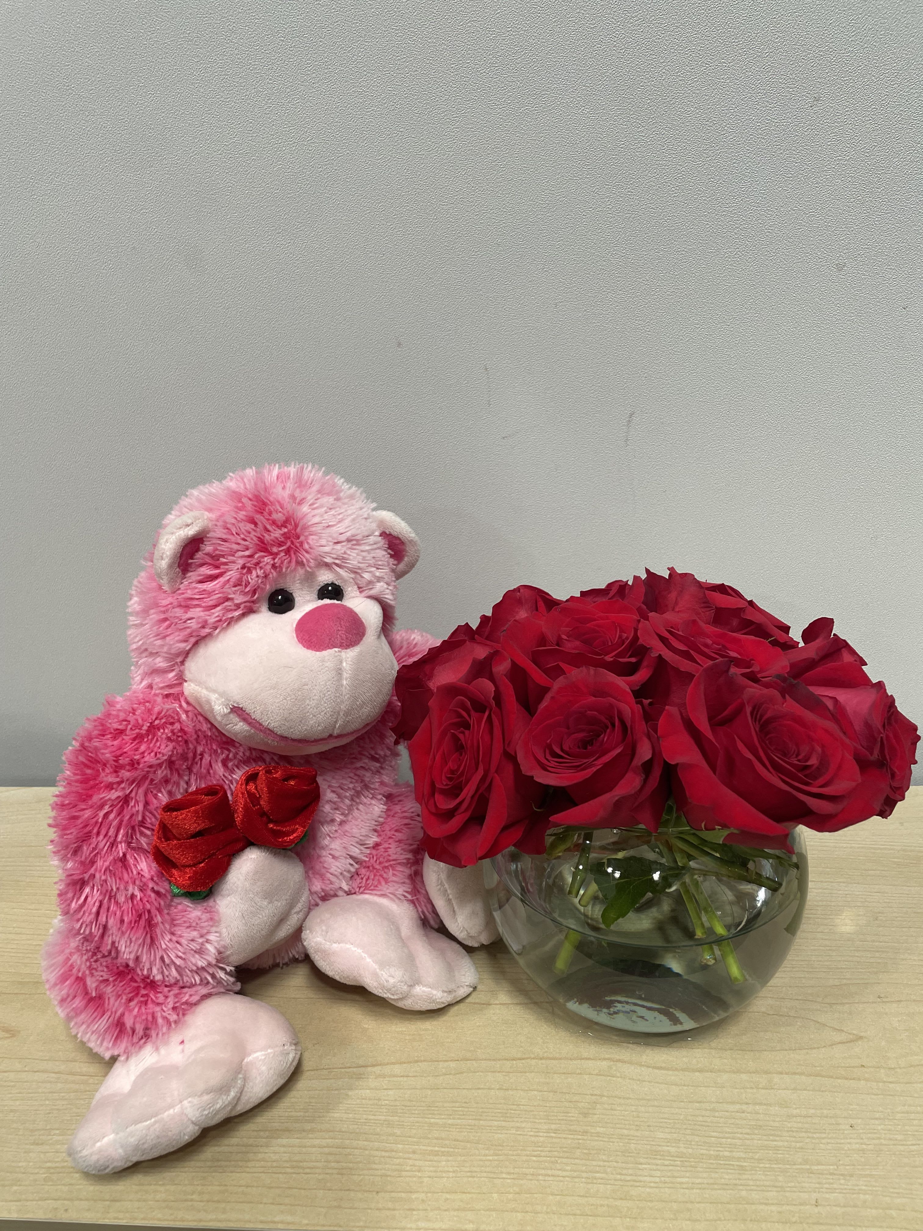 Pink teddy bear beside red roses in a glass bowl vase